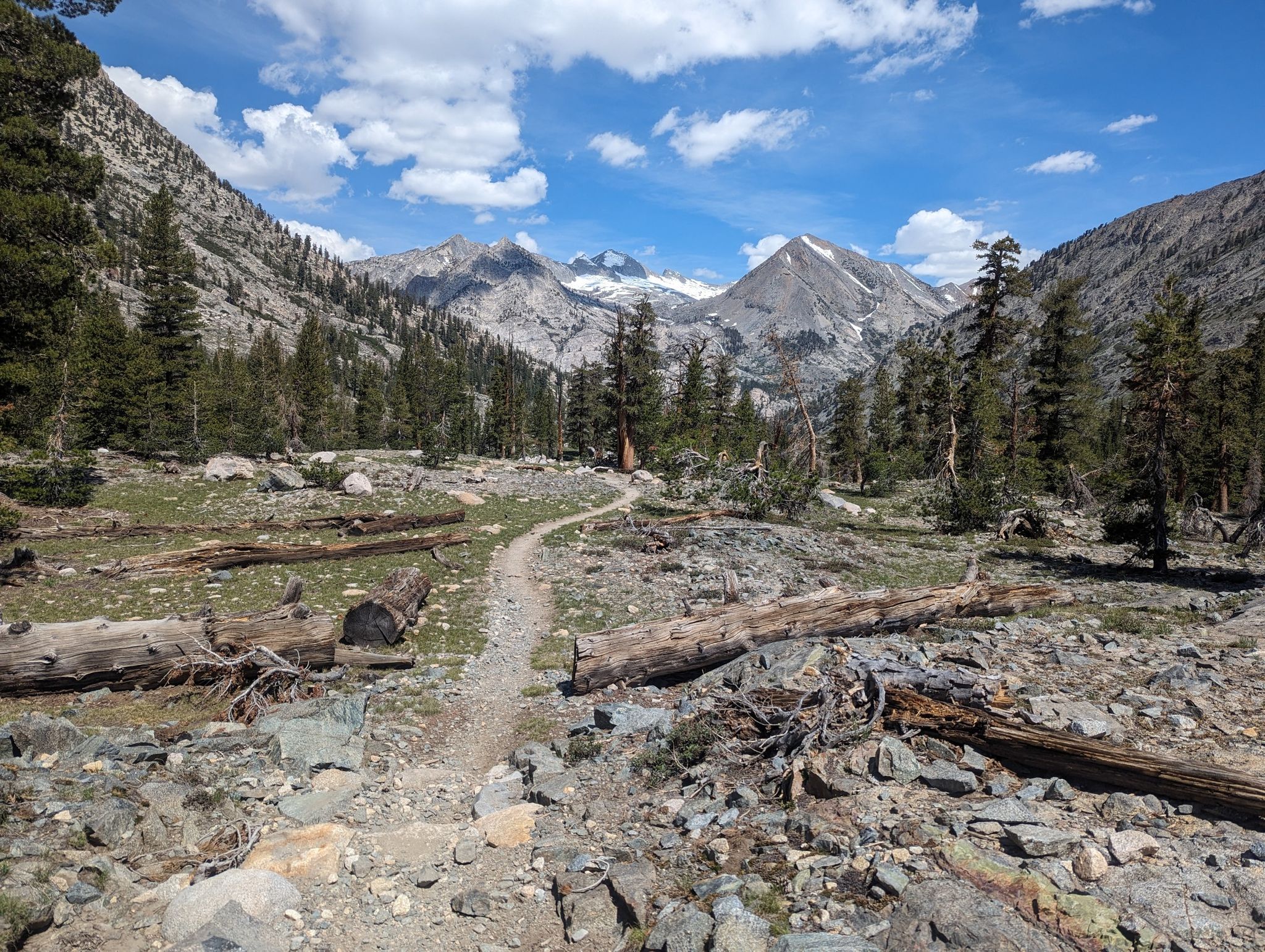 A winding dirt path leads through a rocky valley towards distant mountains. - Rae Lakes Loop