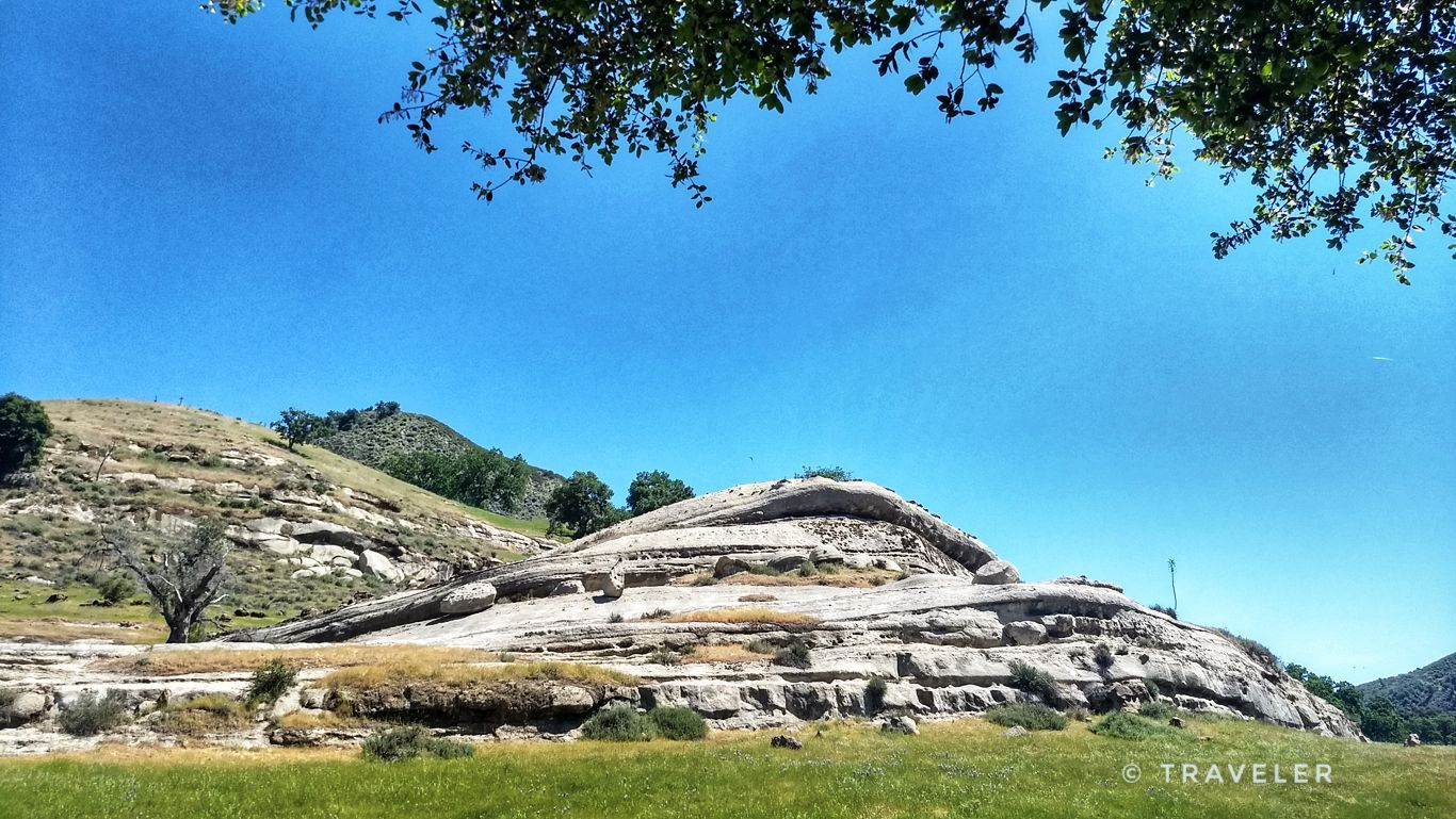 Large layered rock formation in a grassy field under a bright blue sky. - Arroyo Seco - Indians Road