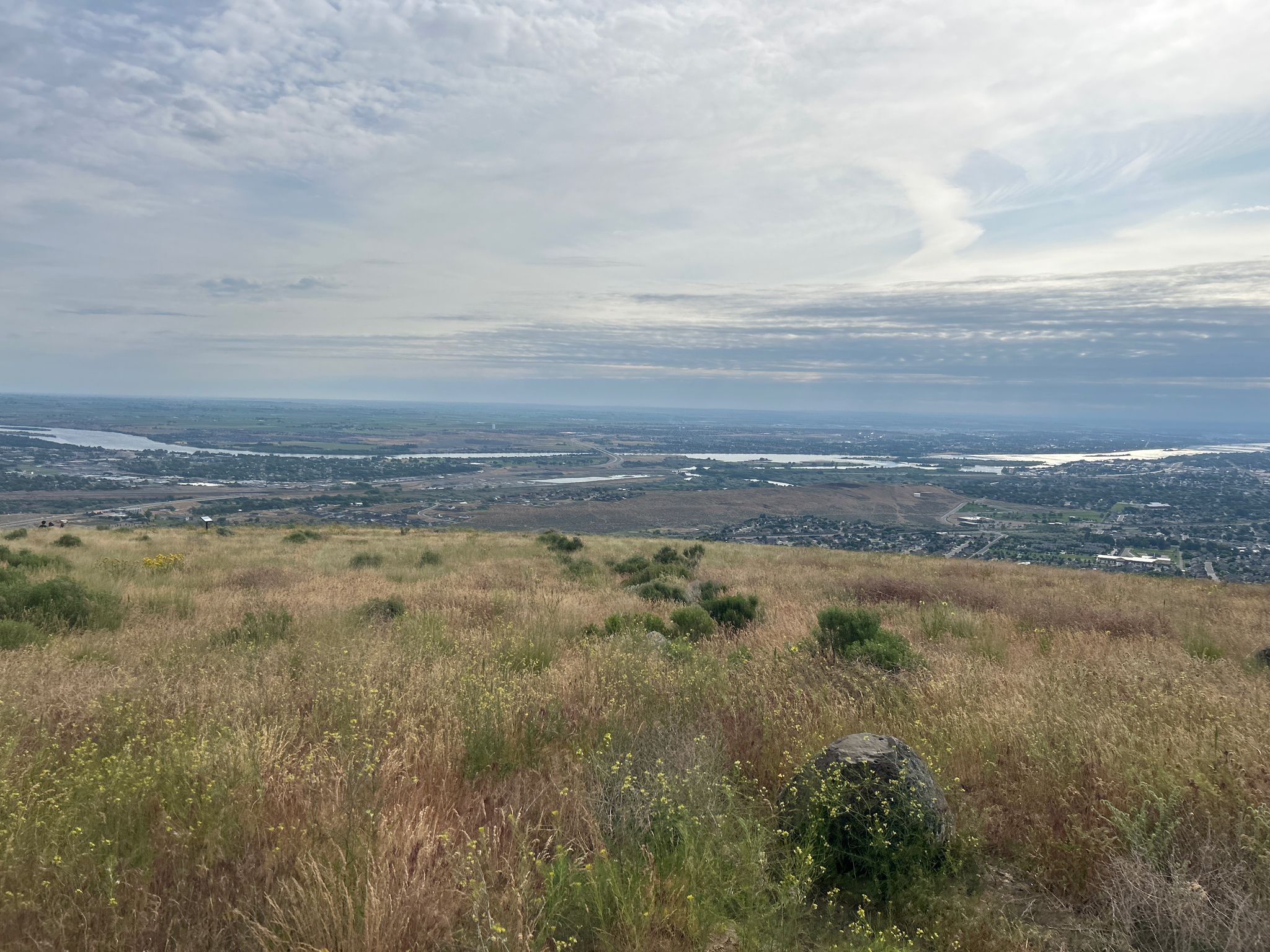 Grassy hillside overlooking a distant city and river under a cloudy sky. - Badger Skyline Trail