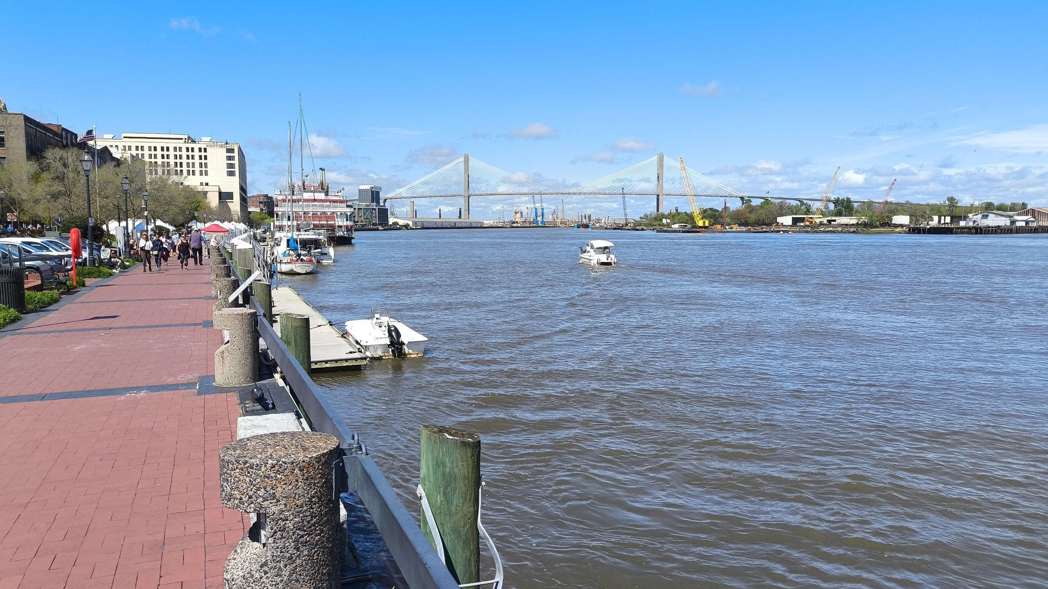 Sunny riverfront with boats, distant bridge, and people walking on a promenade. - Forsyth Park Fountain – Monterey Square loop from Savannah Arts Academy