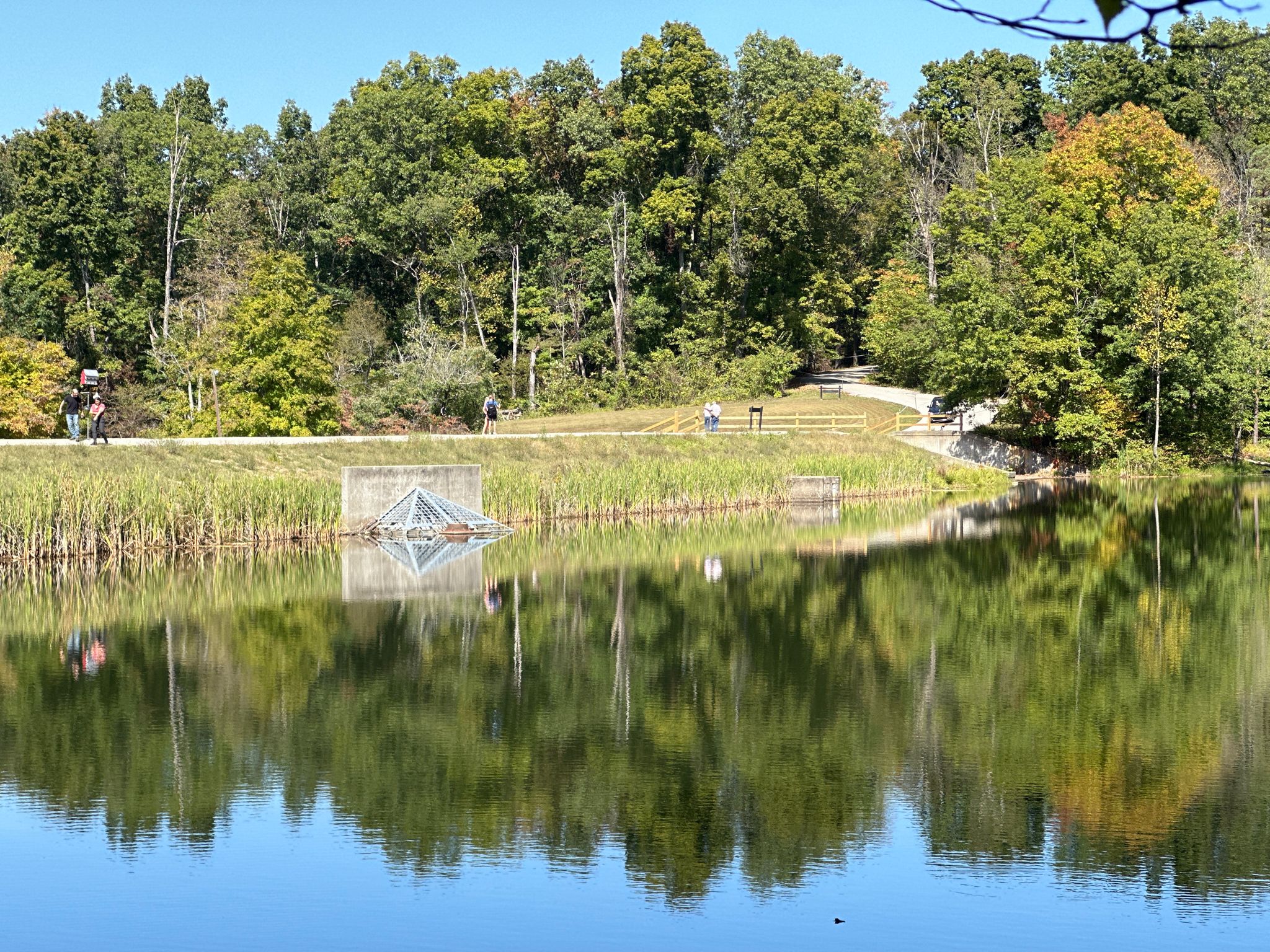 A calm lake reflects green trees and distant people on a sunny day. - Ogle Lake loop from Brown