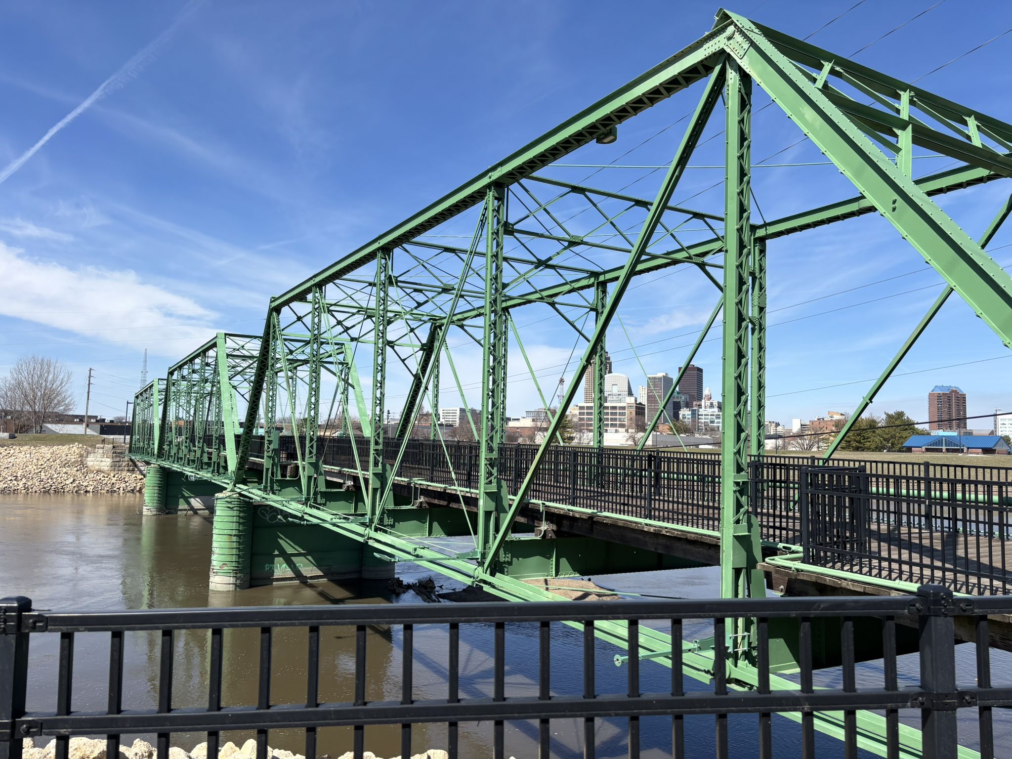 Green metal truss bridge over water on a bright, clear day. - Gray's Lake Park – Gray's Lake beach loop from Des Moines
