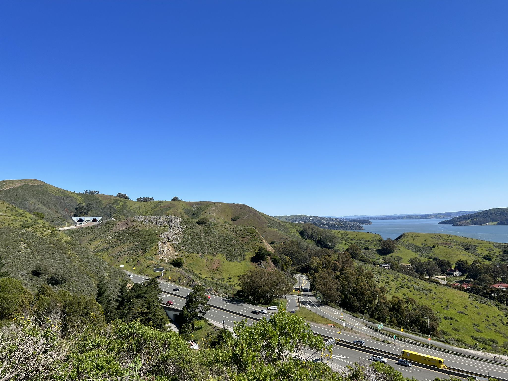 Sunny view of a highway winding through green hills, with a bay. - Golden Gate Bridge – Coastal Trail loop from Marin City