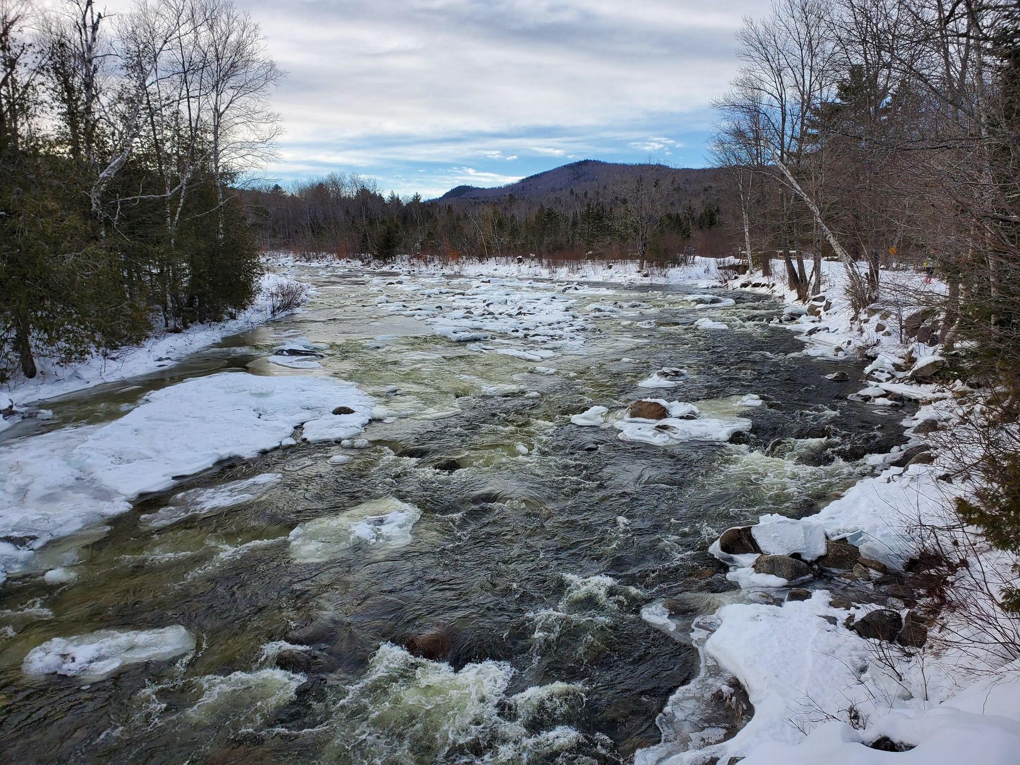 Icy river flows through a snowy winter forest under an overcast sky. - Maine Huts Trail Loop