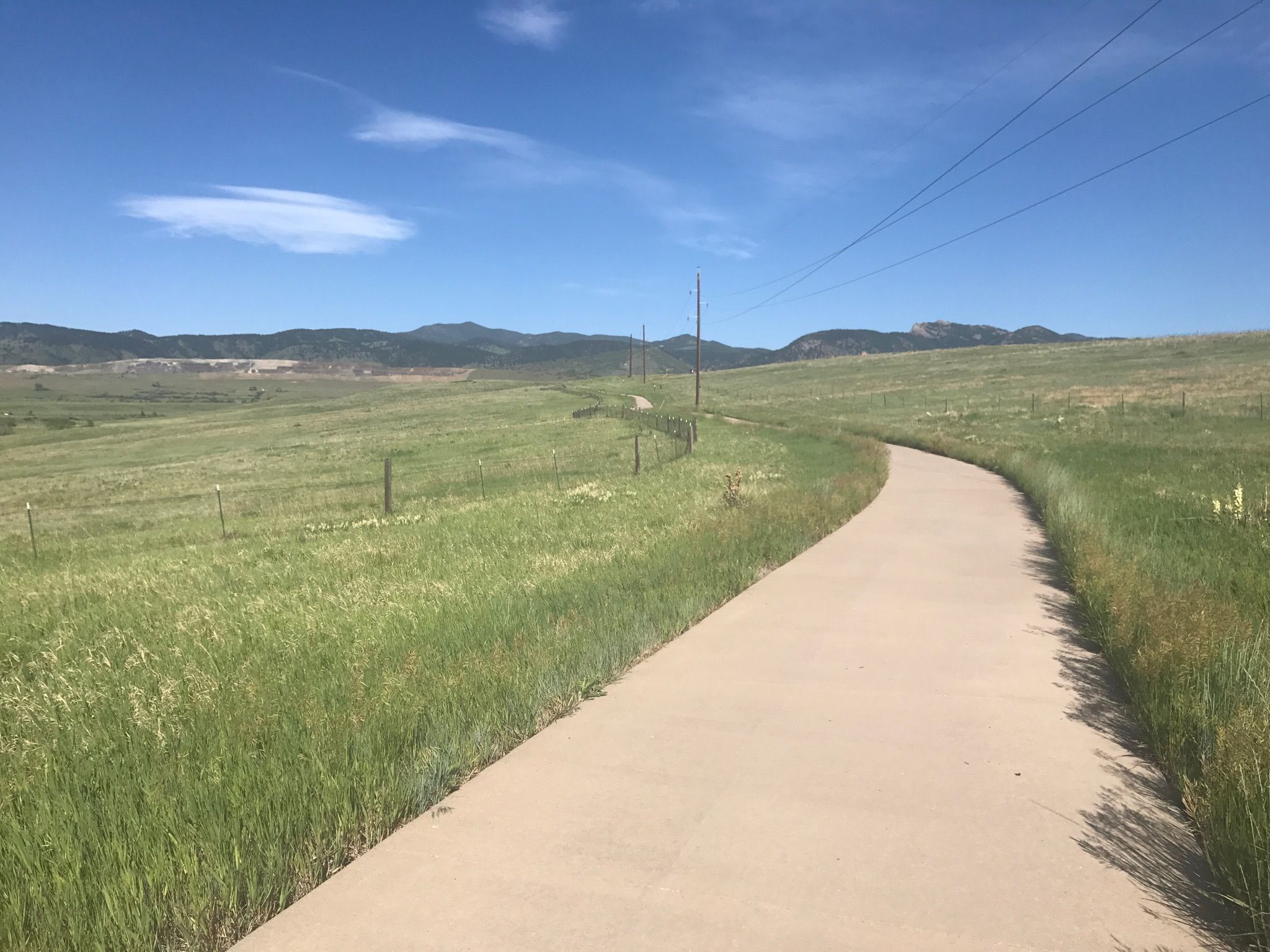 Paved path winding through green fields under a bright blue sky. - Tucker Lake Bench – View of the Arvada Blunn Reservoir loop from Arvada