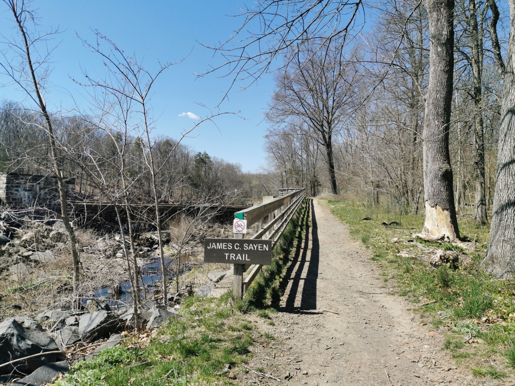 A dirt path runs beside a wooden fence and stream on a sunny day. - Lakeside trail loop from Princeton