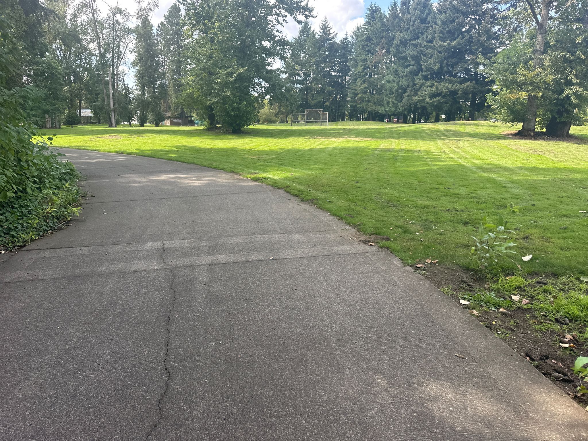 Paved path next to a large green grassy field with distant trees. - Bridge crossing Burnt Bridge Creek – Wintler Park loop from Vancouver Lake Park