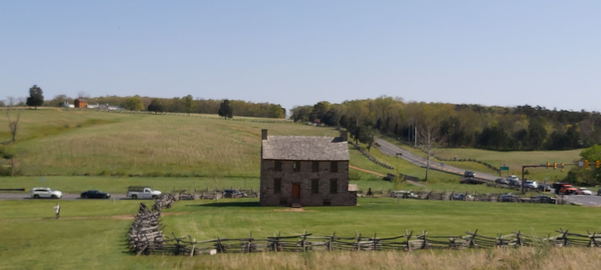 Stone house in a green field with a split rail fence under a clear sky. - First Manassas Trail