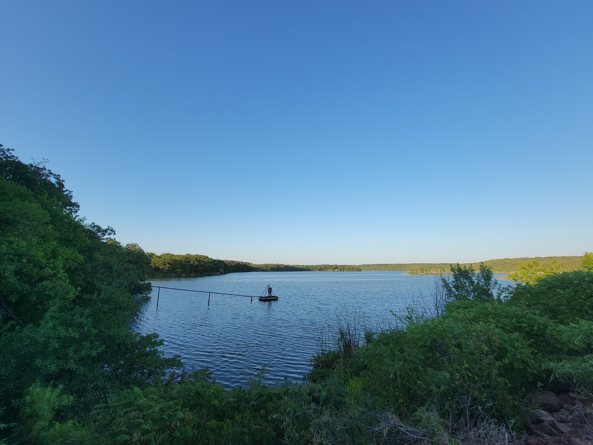 Wide lake view with a person on a small dock, surrounded by green trees. - Cross Timbers Trail Loop