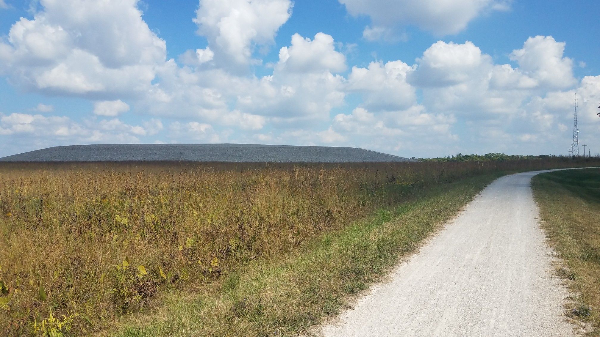 A gravel path curves through a vast field towards a distant hill. - Historic Bridge – Defiance loop from Weldon Spring Heights