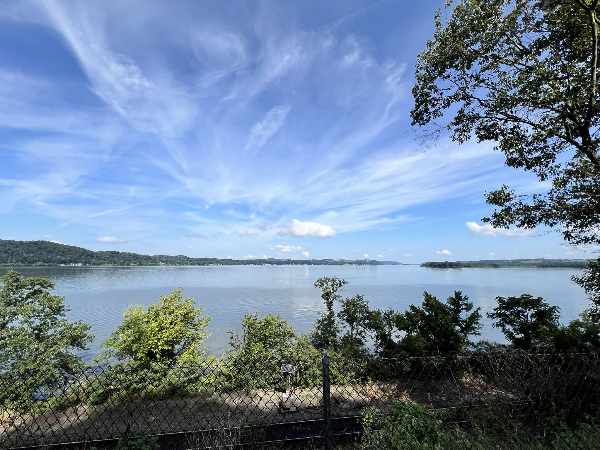 Expansive lake under a bright blue sky with scattered clouds, green trees. - Enola Low Grade Trail