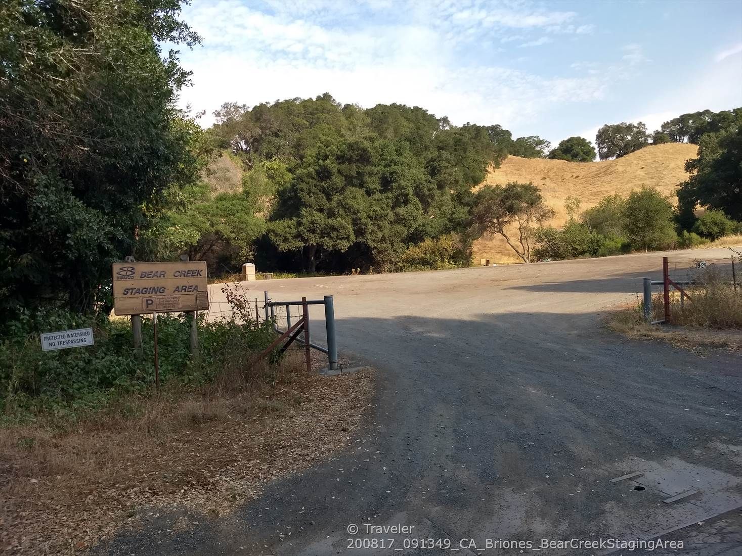 Dirt road entrance to a staging area with dry hills and green trees. - Oursan Trail to Hampton Trail