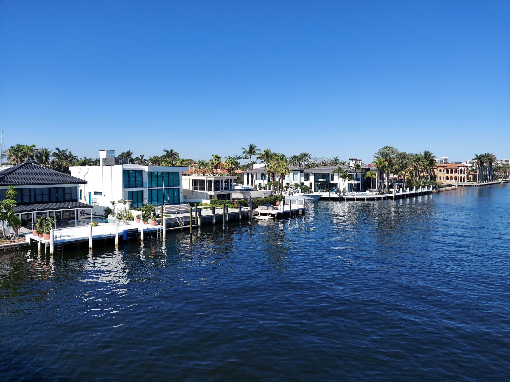 Modern waterfront houses with docks along a calm river under a clear sky. - Las Olas and East Coast Greenway Loop