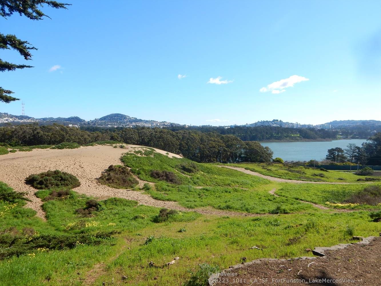 Grassy and sandy hills overlooking a lake and distant city on a sunny day. - Fort Funston Coastal Trail