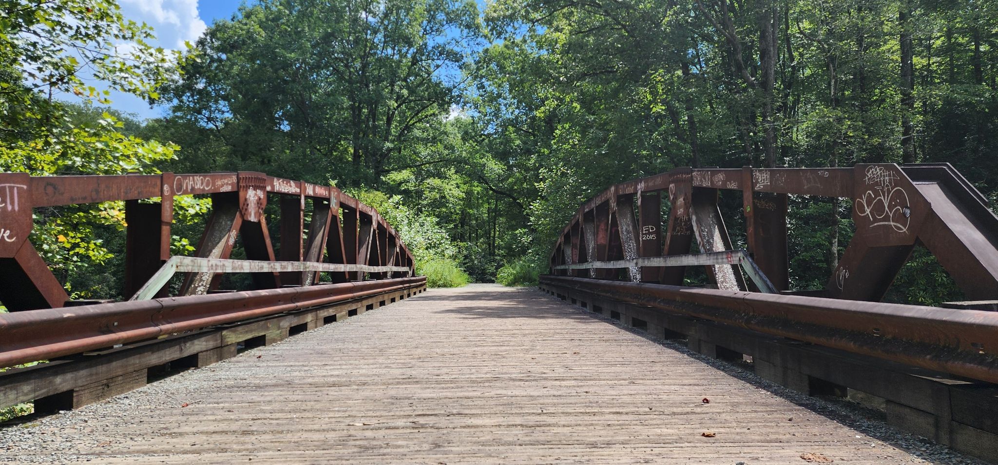 Two rusty metal truss bridges with wooden decks, surrounded by green trees. - Farlow Gap and Daniel Ridge Loop