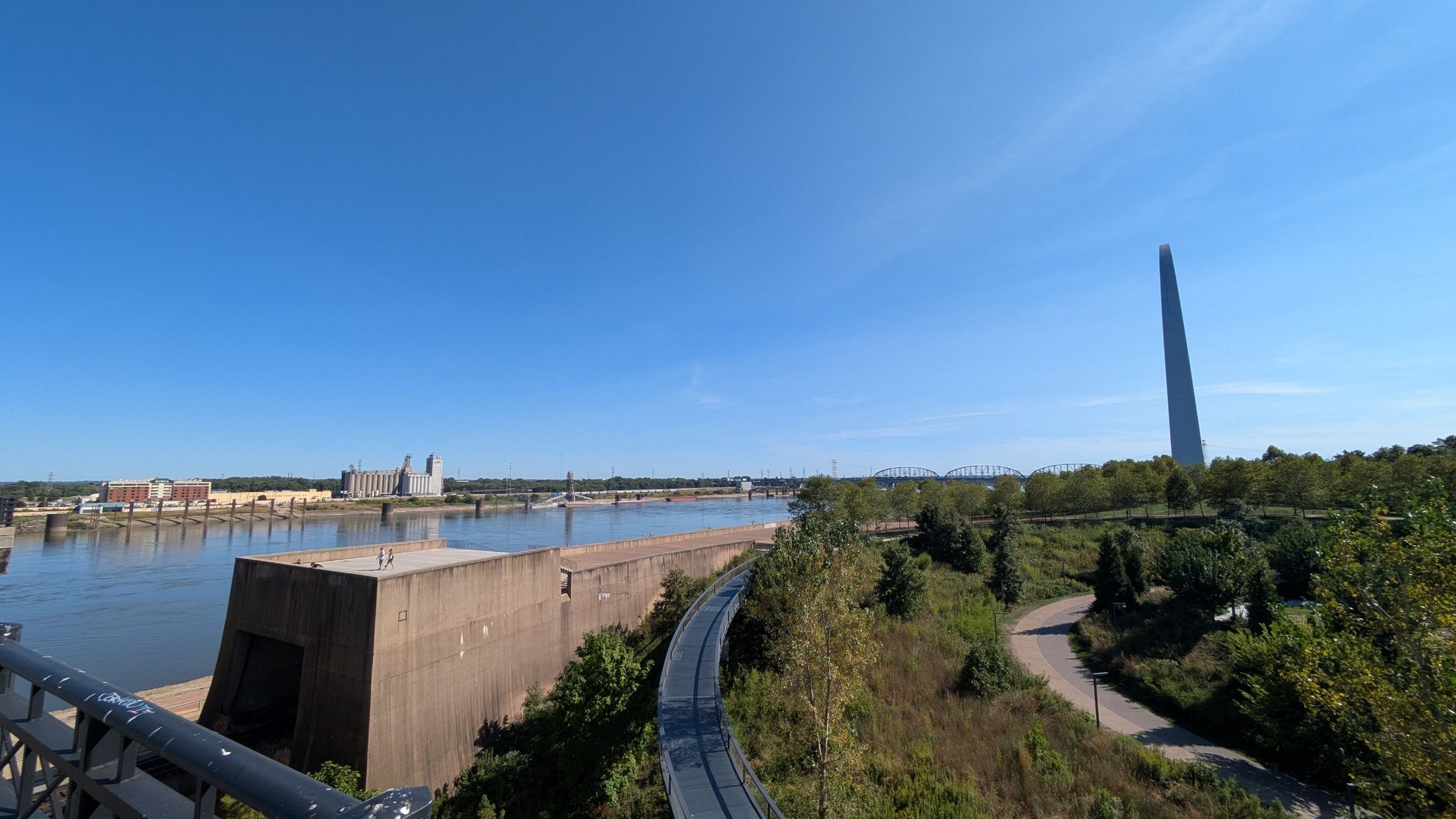 Tall, slender monument overlooking a wide river and distant city. - Gateway Arch – Eads Bridge loop from Union Station