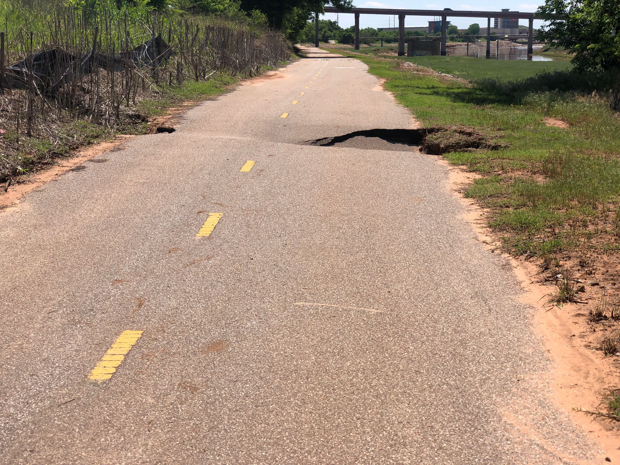 Paved path with a large sinkhole and broken asphalt under bright daylight. - Eagle Lake Trail