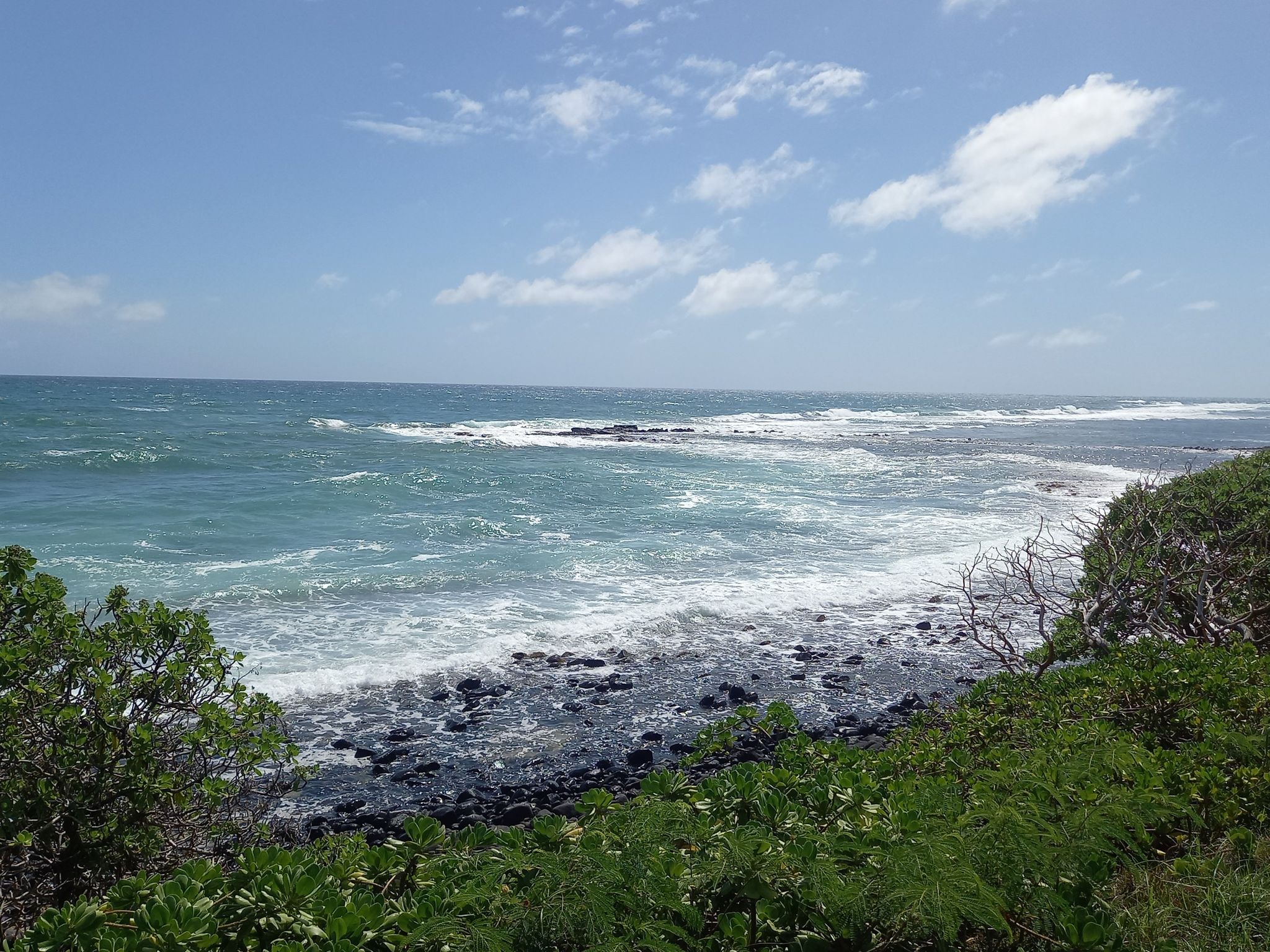 Rough ocean waves crashing on a rocky shore under a bright blue sky. - Kapaa Bike Path – Keālia Beach loop from Wailua