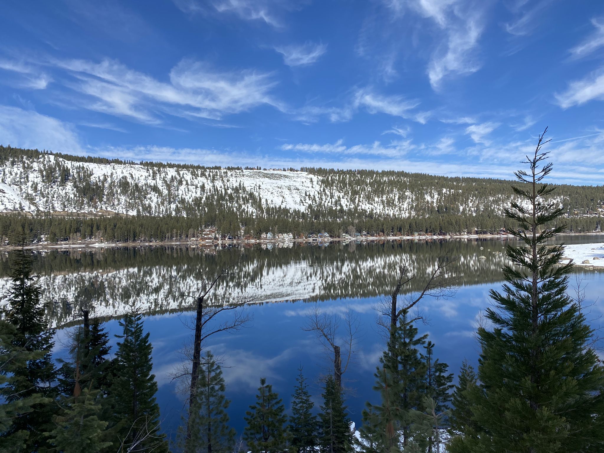 Snowy mountains reflecting in a calm lake under a blue sky with pine trees. - Tahoe-Pyramid Bikeway and Donner Pass Loop