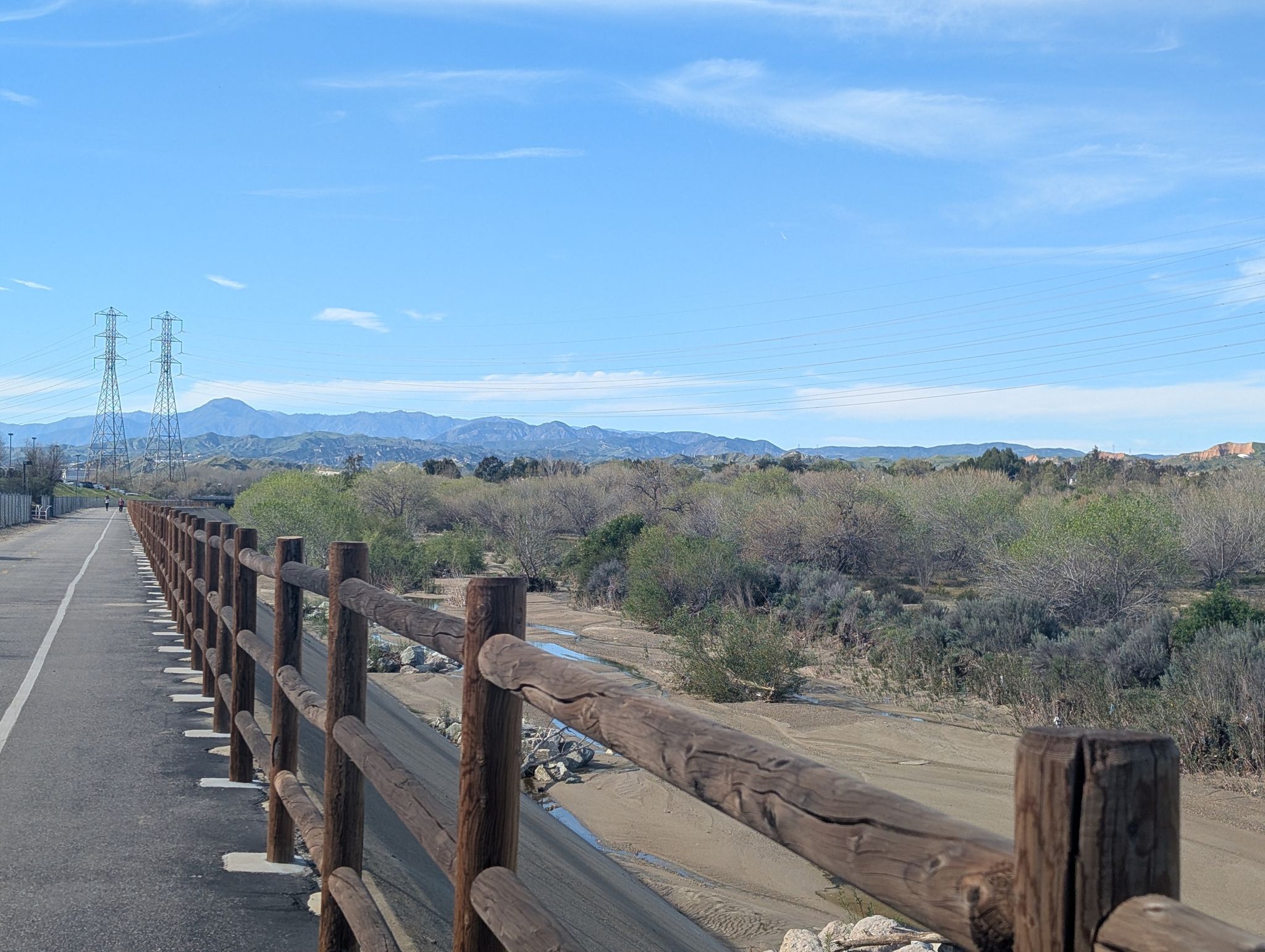 Paved path with wooden fence alongside a dry riverbed under a clear blue sky. - Santa Clara River and San Francisquito Creek Trail Loop