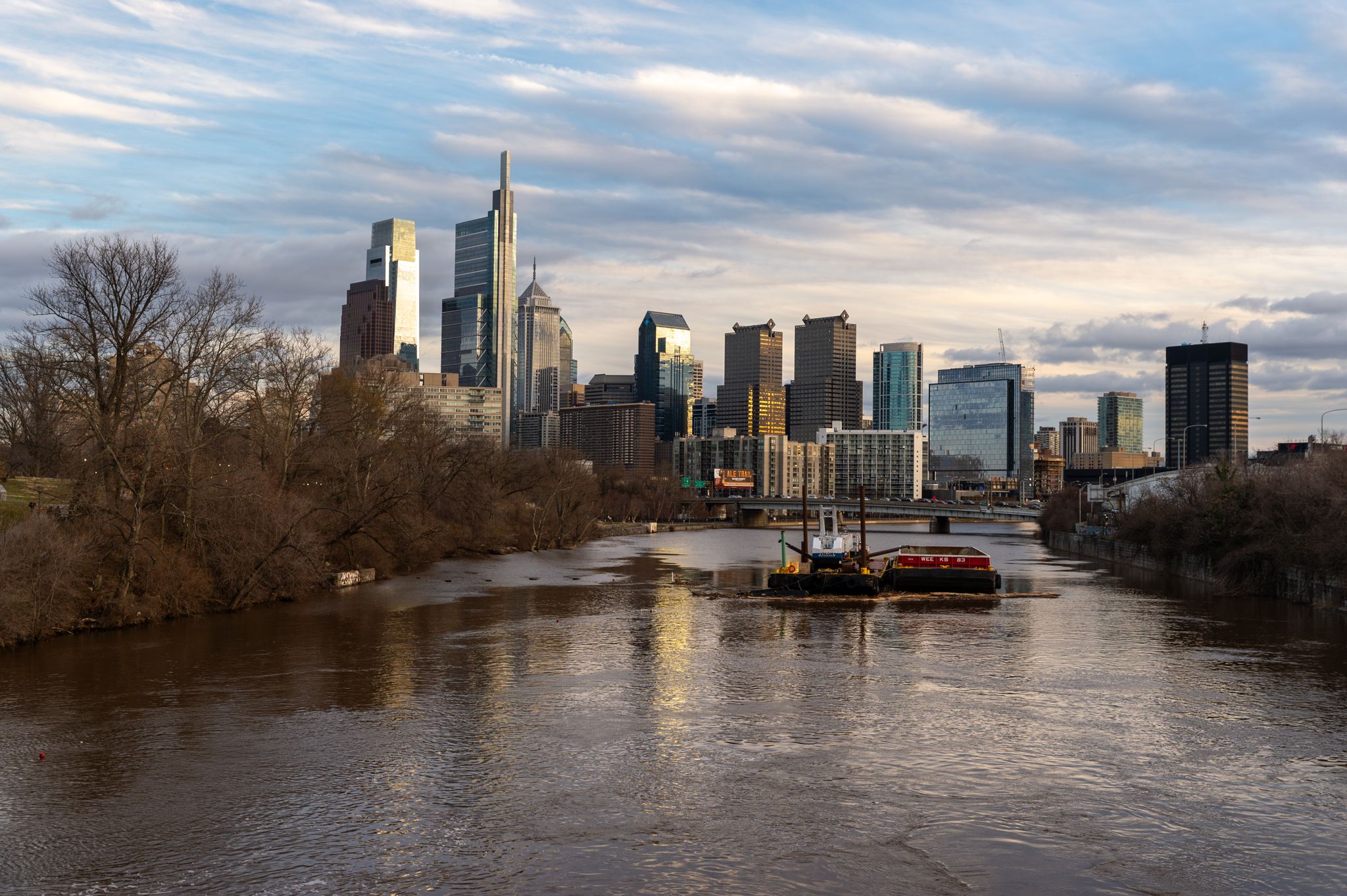 City skyline, river with barge, bare trees under cloudy golden light. - Schuylkill River Trail Loop