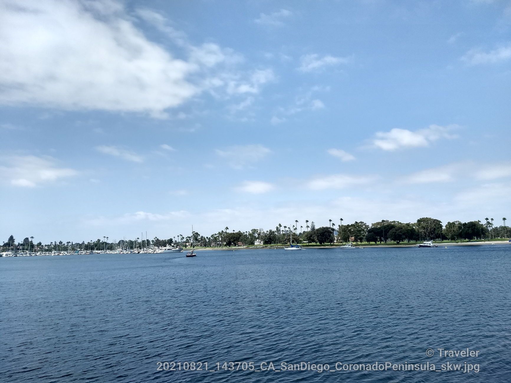 Wide blue water with distant shoreline, trees, buildings, and boats. - Silver Strand State Beach loop from Coronado Cays