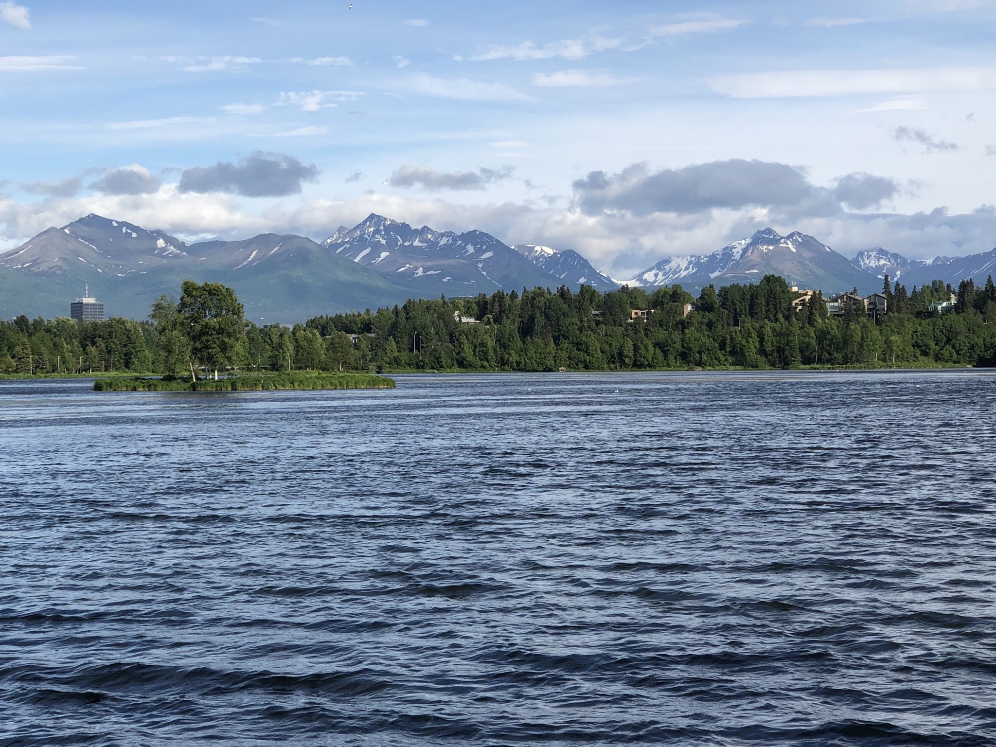 Large lake with an island, green trees, and distant snow-capped mountains. - Westchester Lagoon – Westchester Lagoon loop from Sullivan Arena