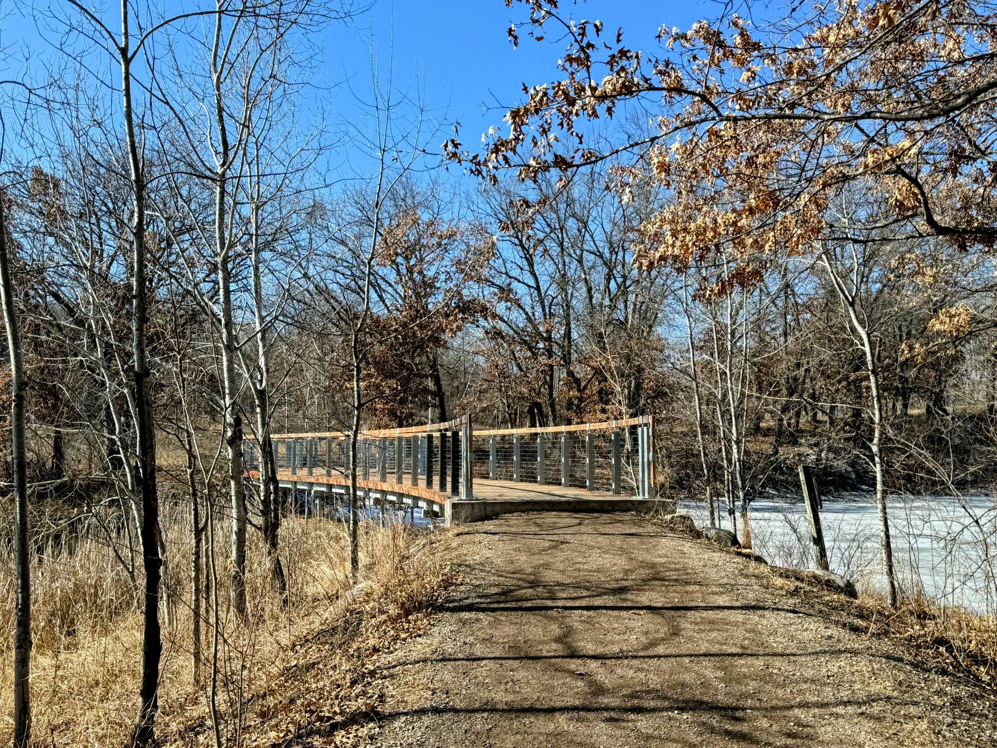 Curved modern bridge over a partially frozen body of water, with bare trees. - McDonough Lake – Portage Lake loop from Lebanon Hills Regional Park Visitor Center Overflow Lot