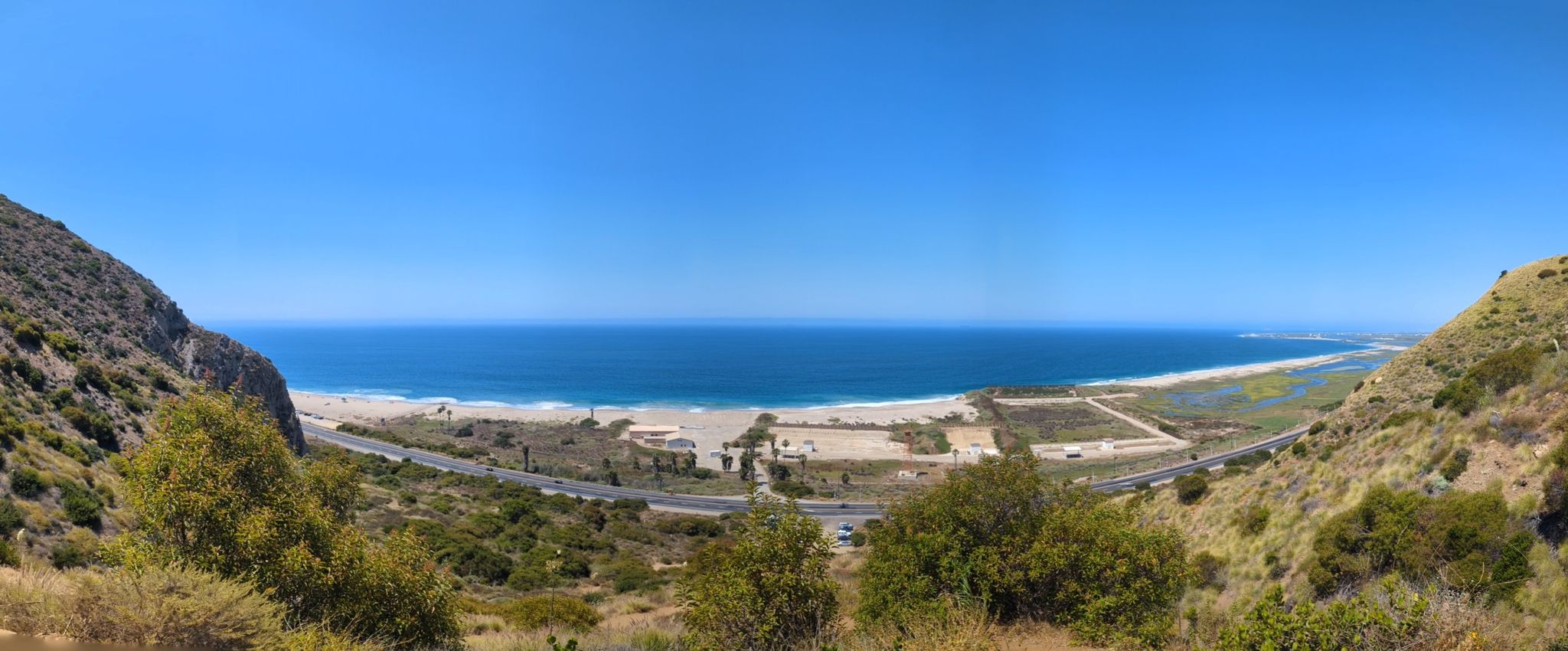 Panoramic view of a sunny beach and ocean from a green hillside. - Mugu Peak and Chumash Trail Loop