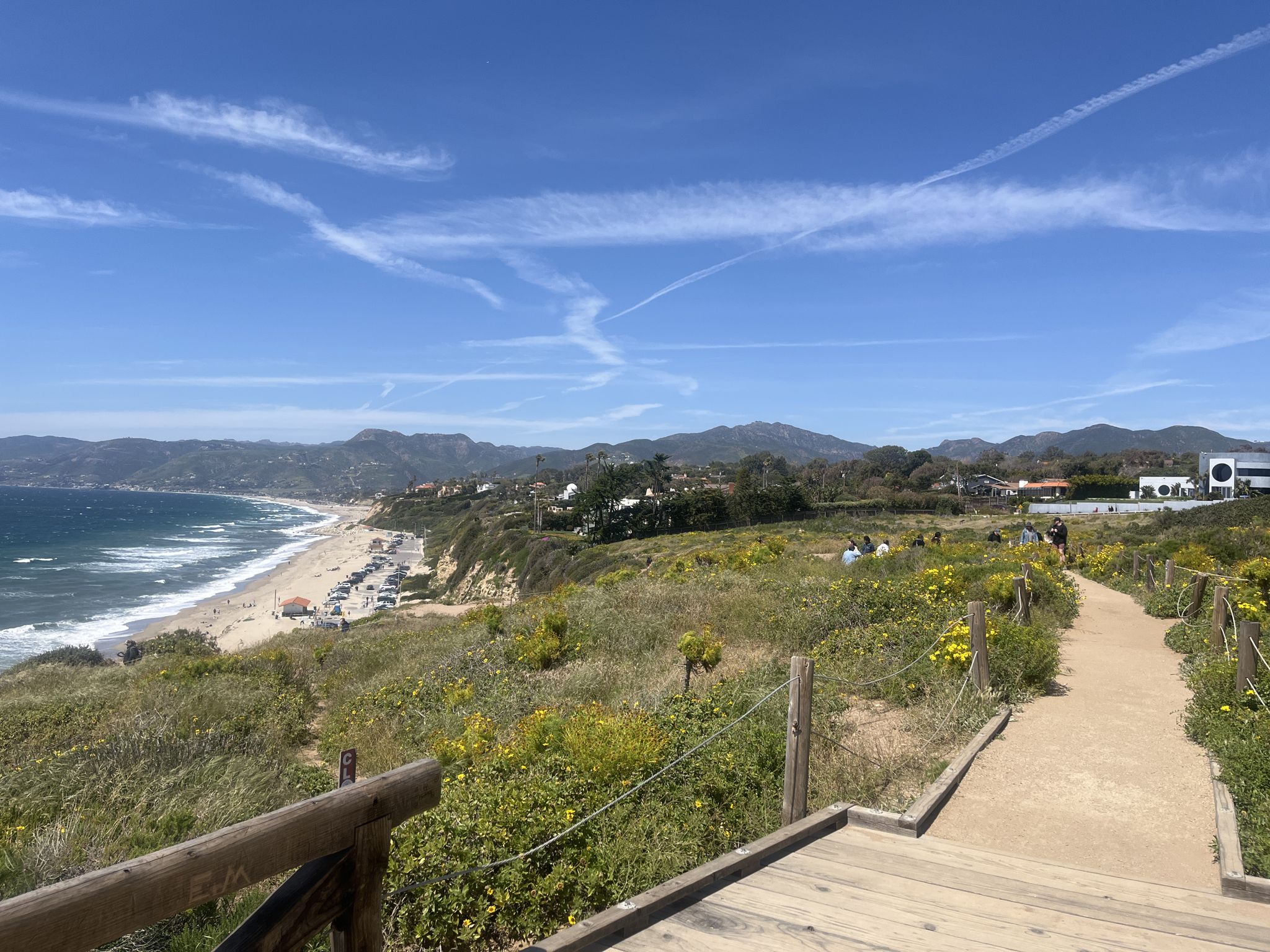 Elevated view of a beach, ocean, mountains, and a wooden pathway under blue sky. - Point Dume Overlook loop from Malibu Riviera