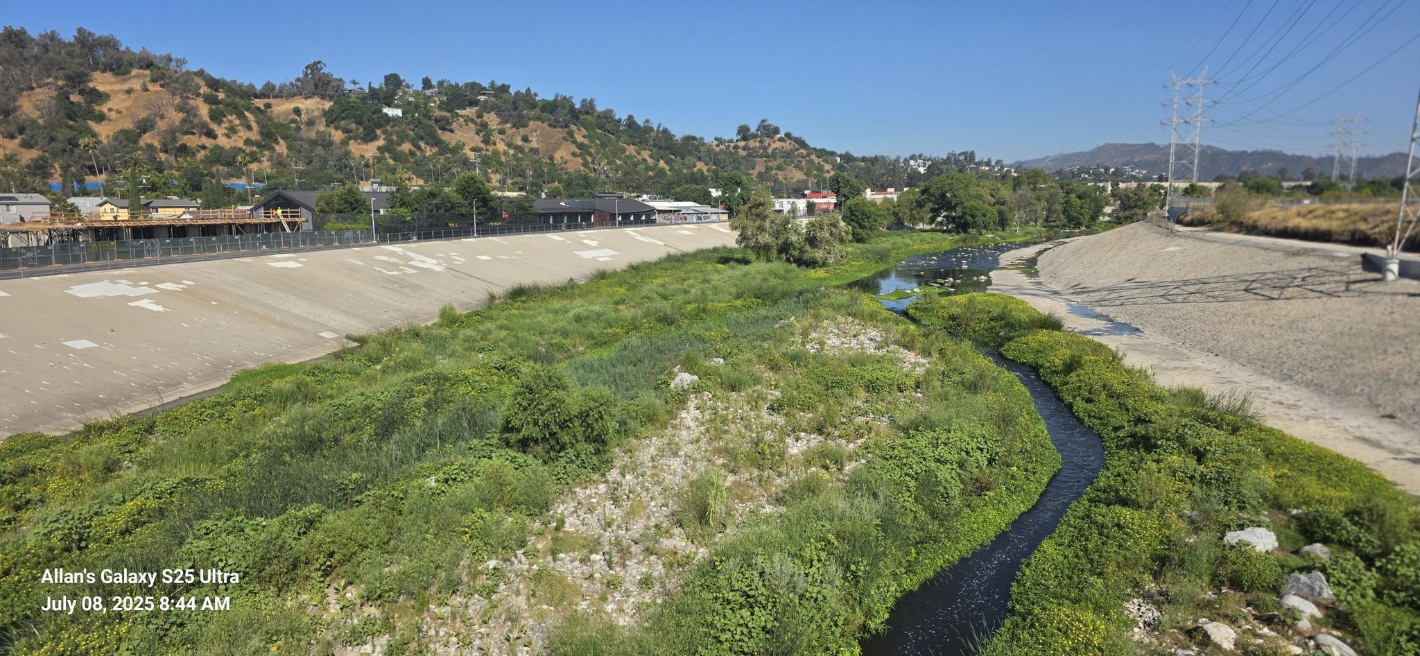 Concrete channel with green island, narrow stream, and distant hills under bright sun. - Baum Bicycle Bridge – View of Eagle Rock loop from Universal City/Studio City