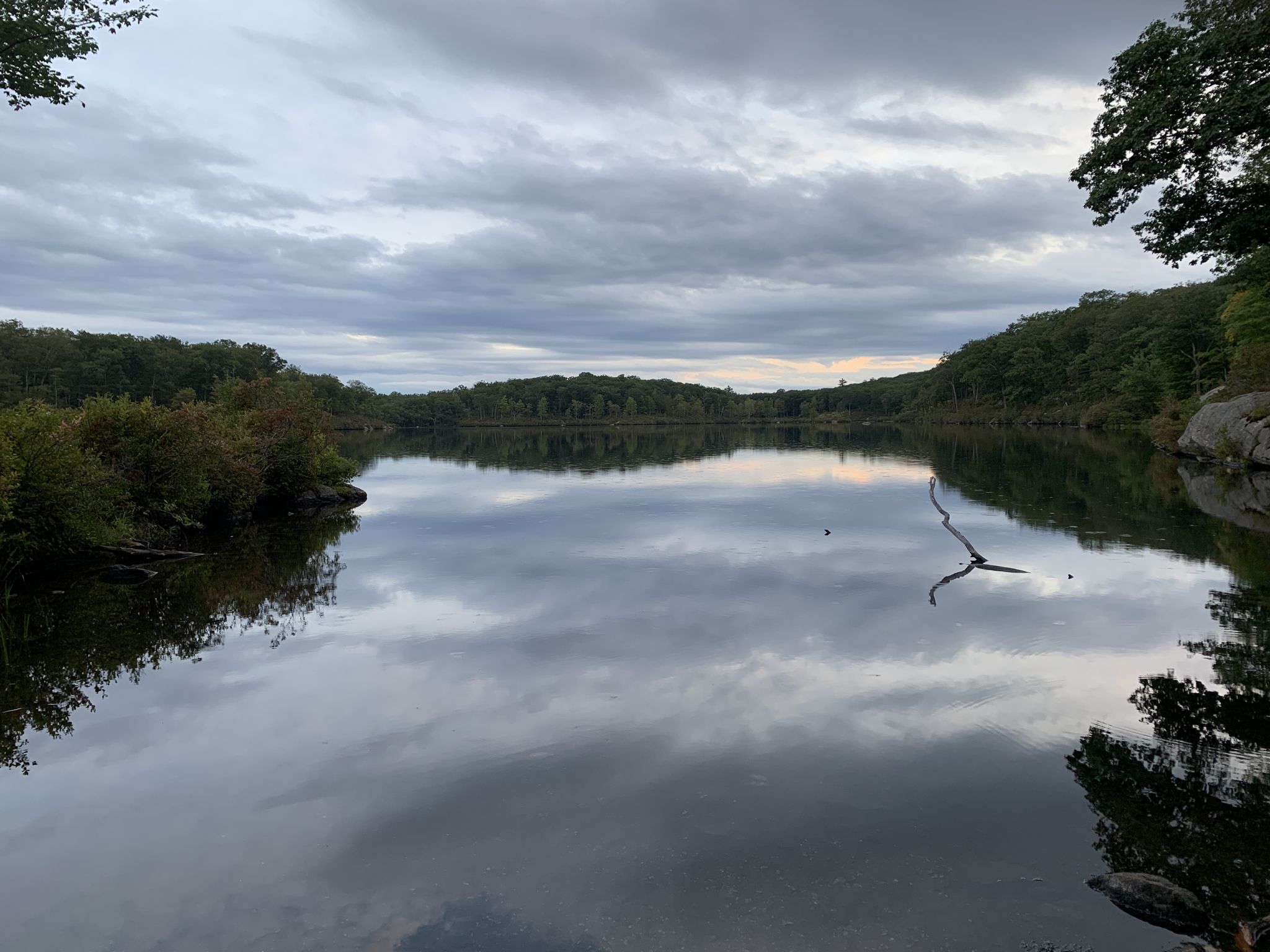 Calm lake reflecting an overcast sky, surrounded by lush green trees. - Parker Cabin Mountain – Claudius Smith's Den loop from Tuxedo