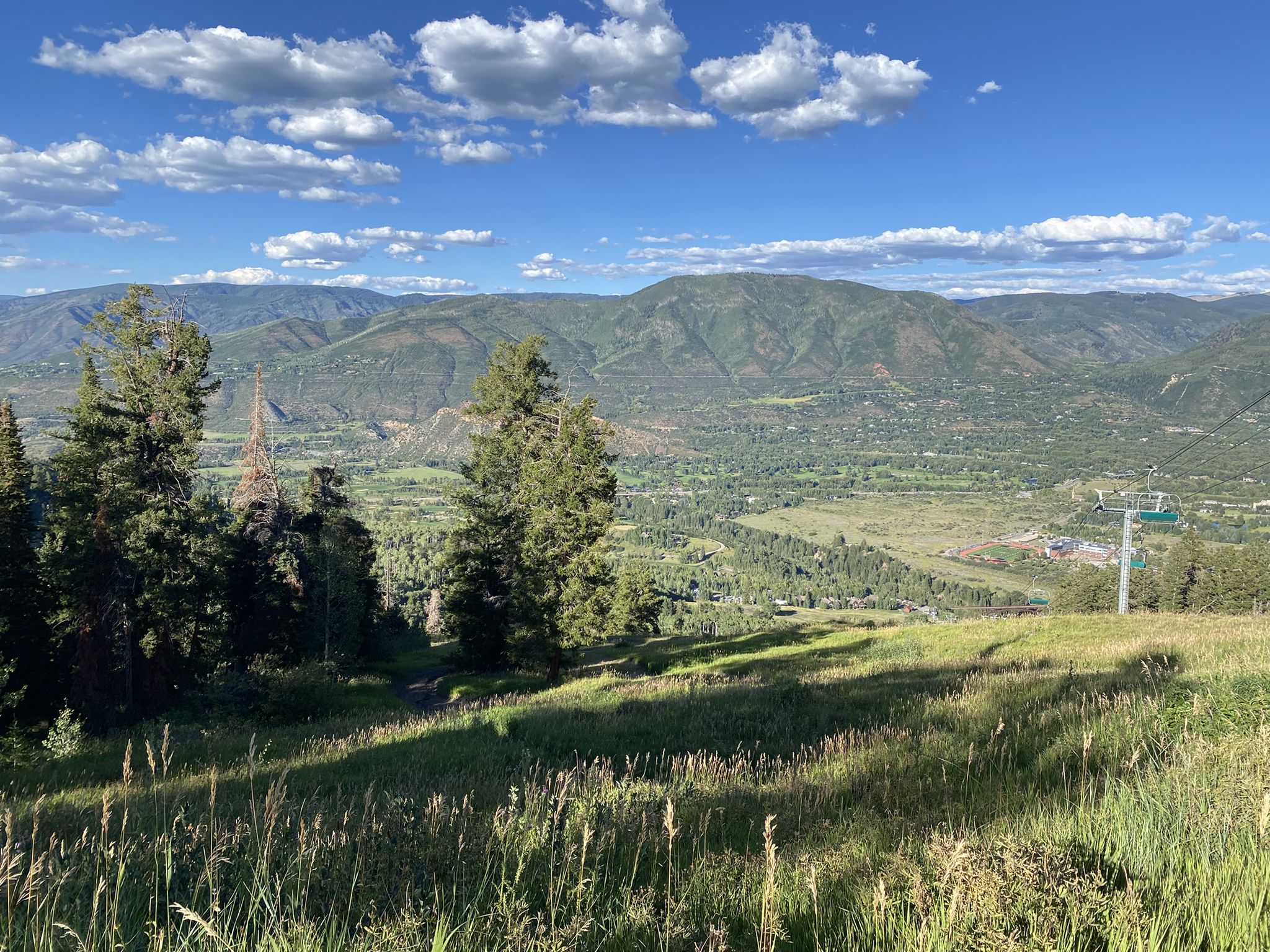 Sunny mountain view with green valley, distant peaks, and a ski lift. - Buttermilk Mountain Trail