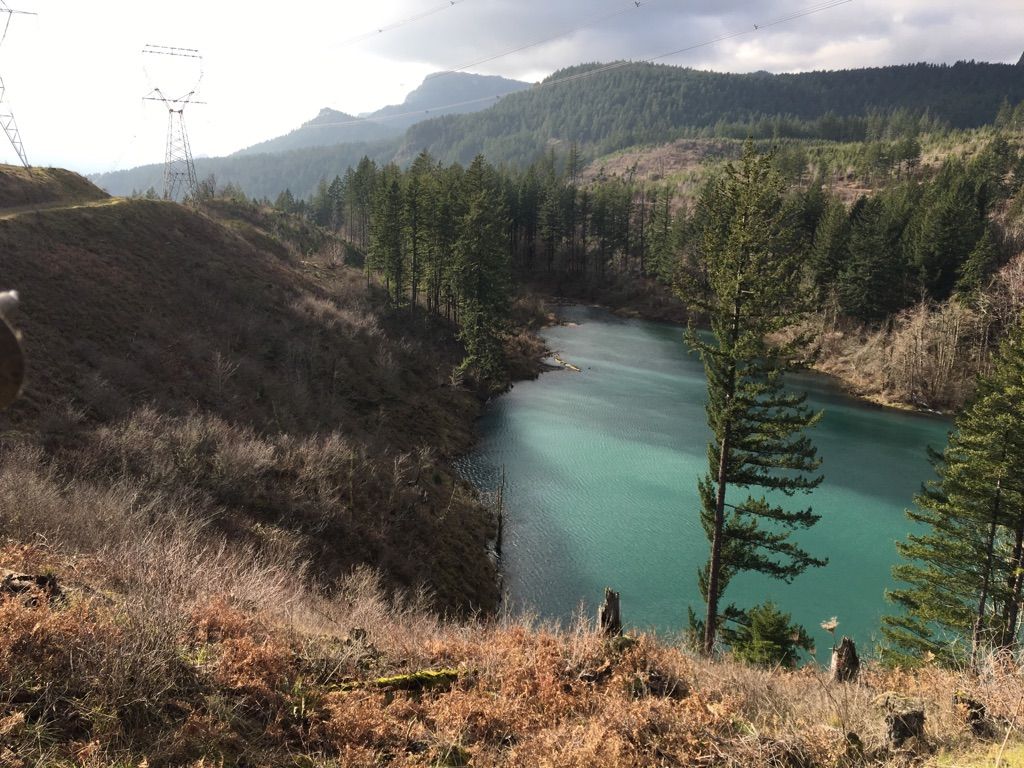 Turquoise lake nestled between hills with power lines under a cloudy sky. - Gillette Lake via Pacific Crest Trail