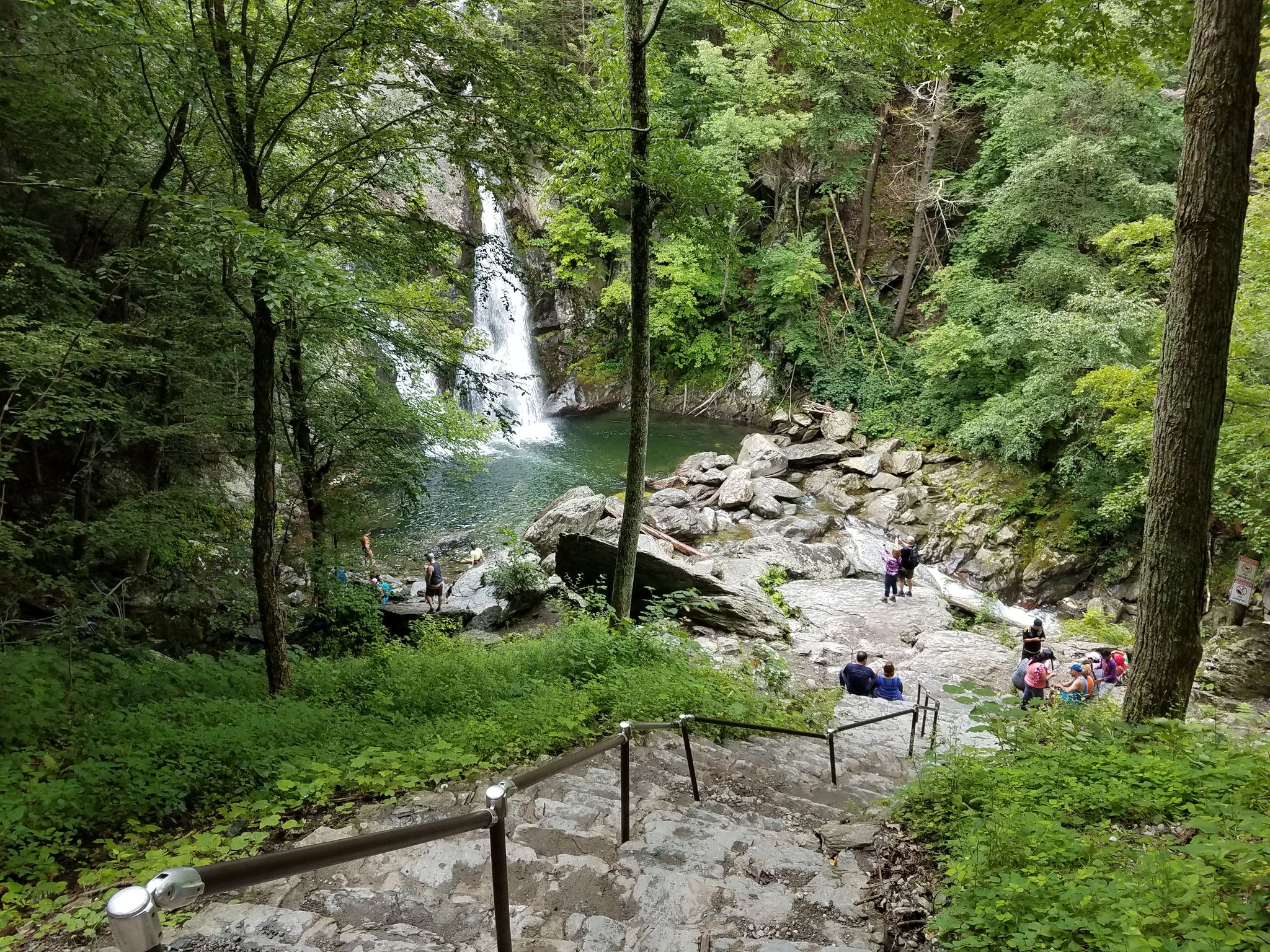 People on stone steps overlooking a waterfall and pool in a green forest. - Taconic State Park – Copake Iron Works Furnace loop from Taconic State Park – Copake Falls Area