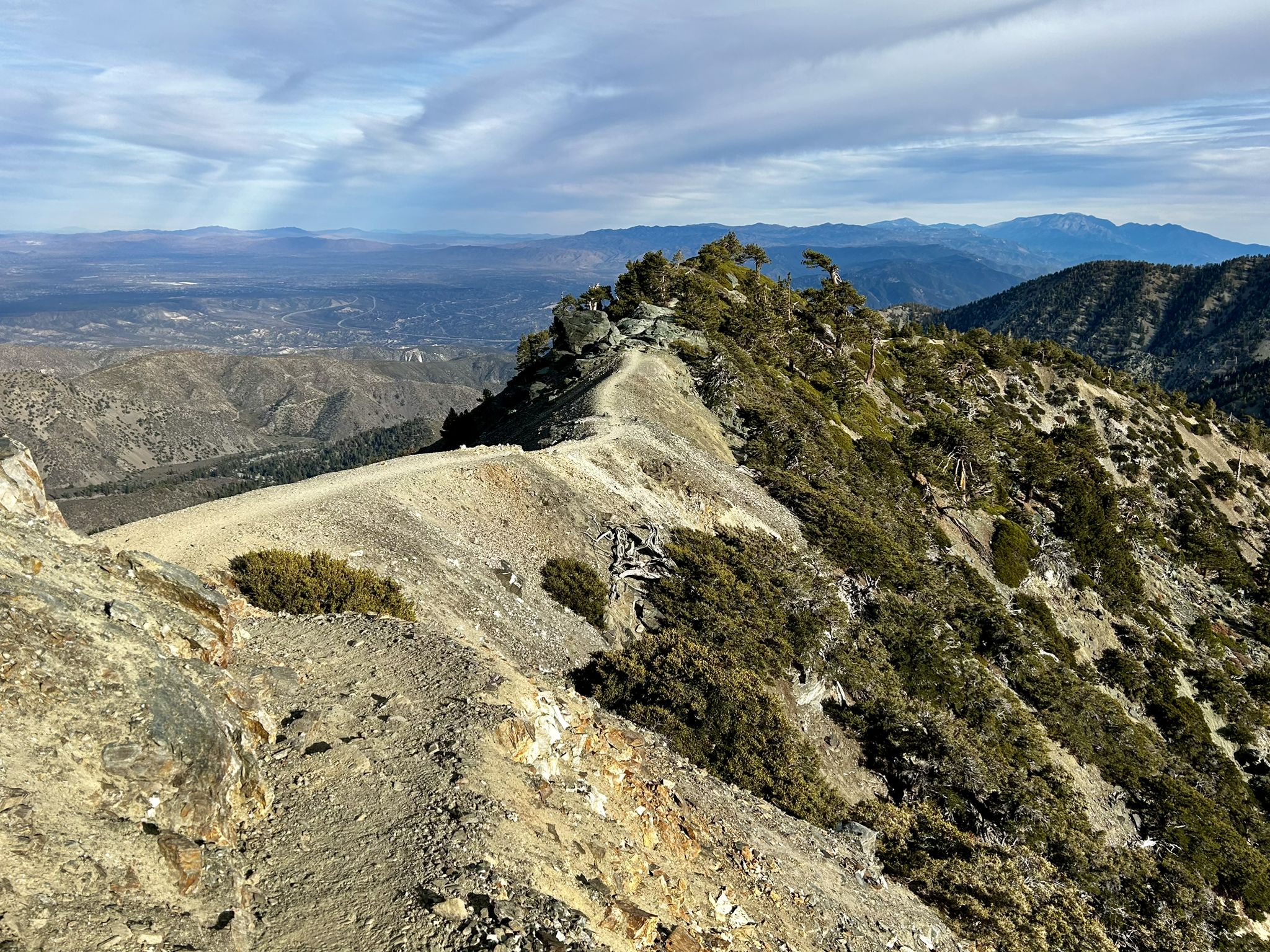 A winding path along a rocky mountain ridge with distant valleys under clouds. - Devil's Backbone Trail loop