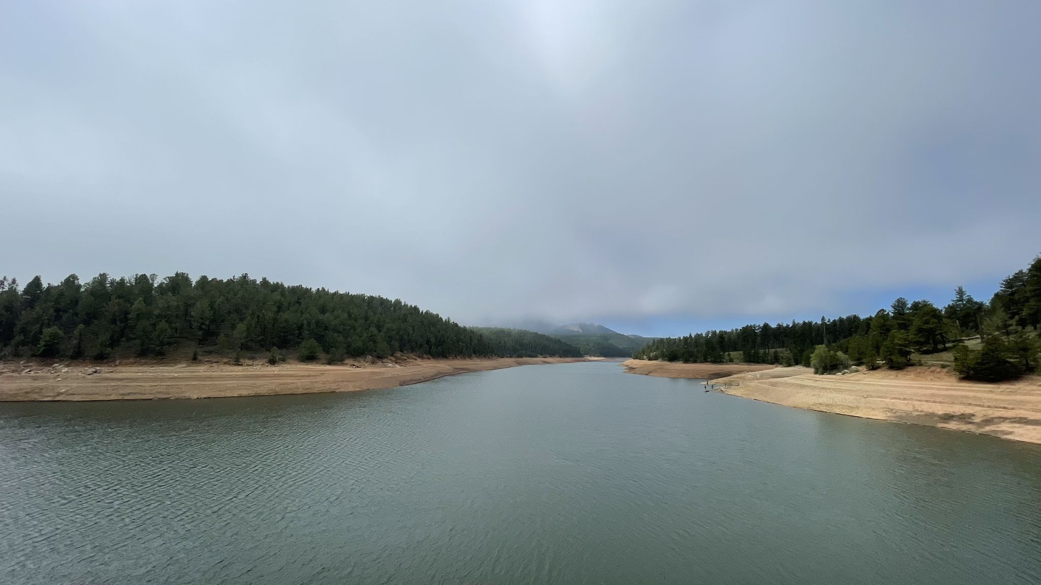 A wide lake with pine forests and sandy banks under an overcast sky. - South Catamount Reservoir