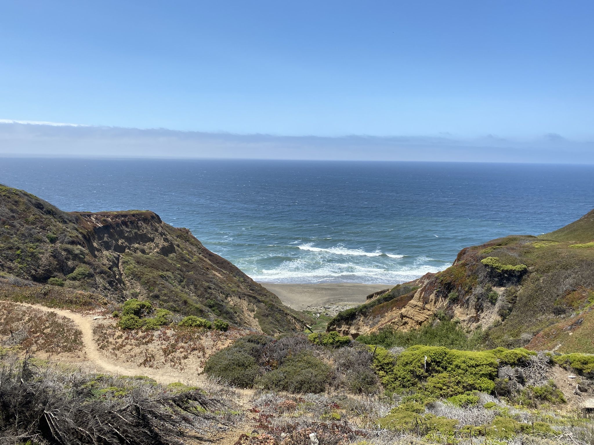Ocean waves crash on a sandy beach between two steep, green cliffs. - Bay Area Ridge Trail: Skyline College to Mussel Rock