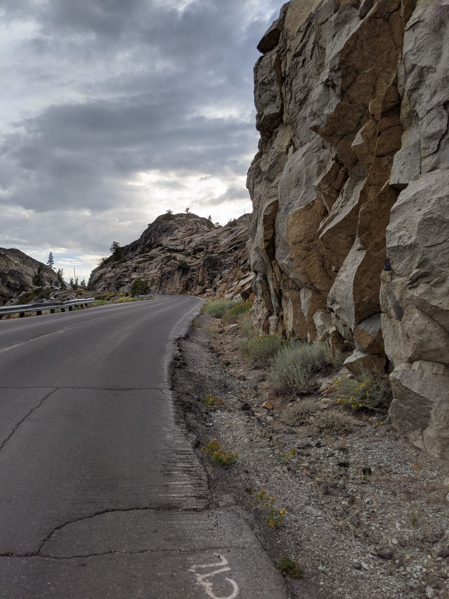 Winding road next to a large rocky cliff under a cloudy sky. - Donner Ski Ranch – View of Donner Lake loop from Cisco Grove