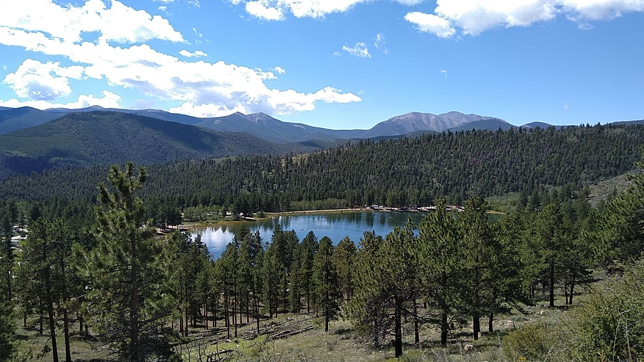 Serene lake surrounded by dense pine forests and mountains under a cloudy blue sky. - Marshall Pass and Poncha Creek OHV Route