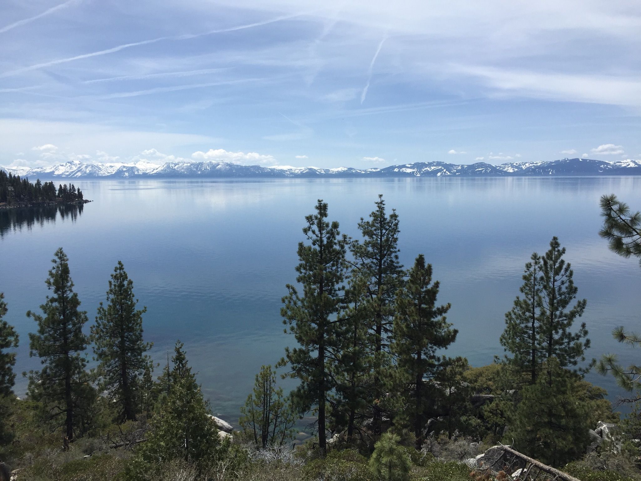 Calm lake reflecting a partly cloudy sky, with distant snow-capped mountains. - Lake Tahoe – Sand Harbor Beach loop from Skunk Harbor