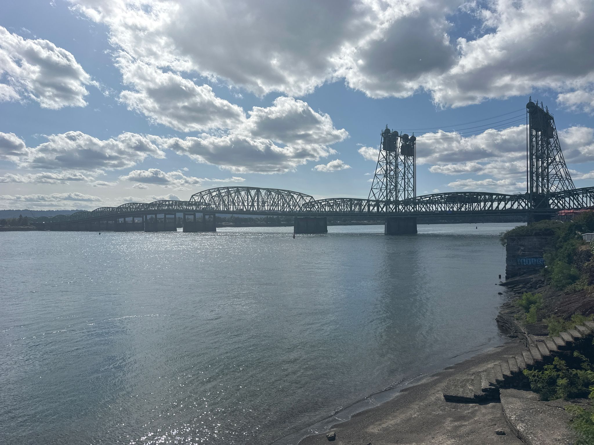 A long metal bridge spans a wide river under a cloudy sky. - Discovery Historic Loop