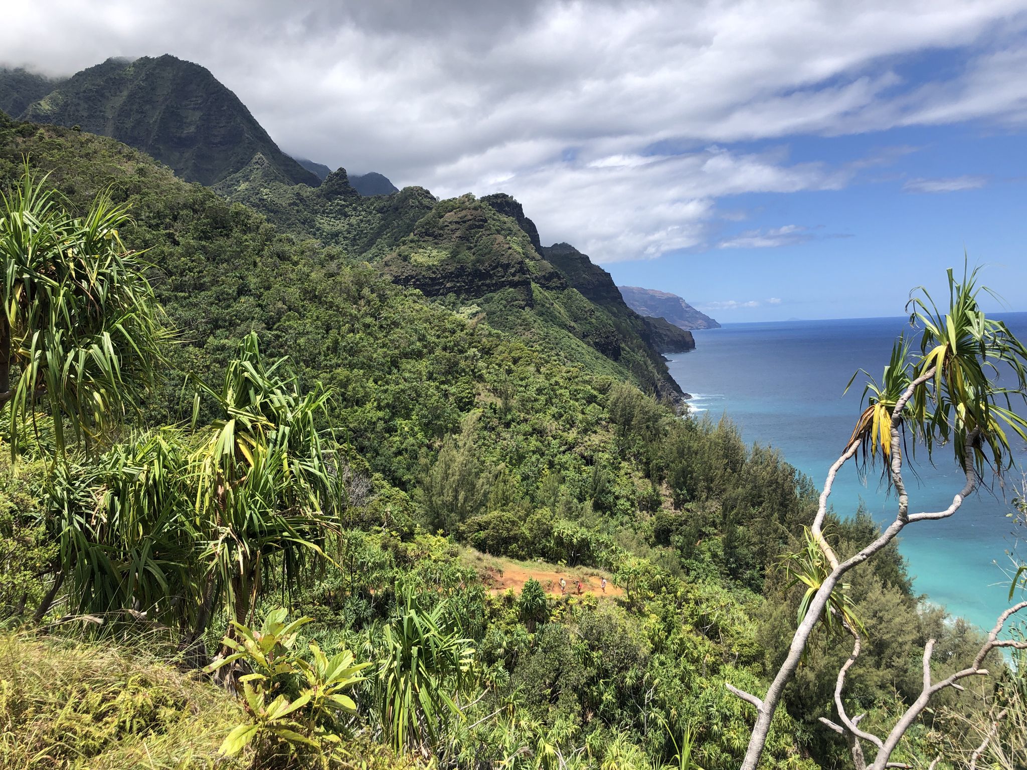 Panoramic view of lush green mountains meeting a turquoise ocean under a cloudy sky. - Kalalau Trail to Hanakapiʻai Beach