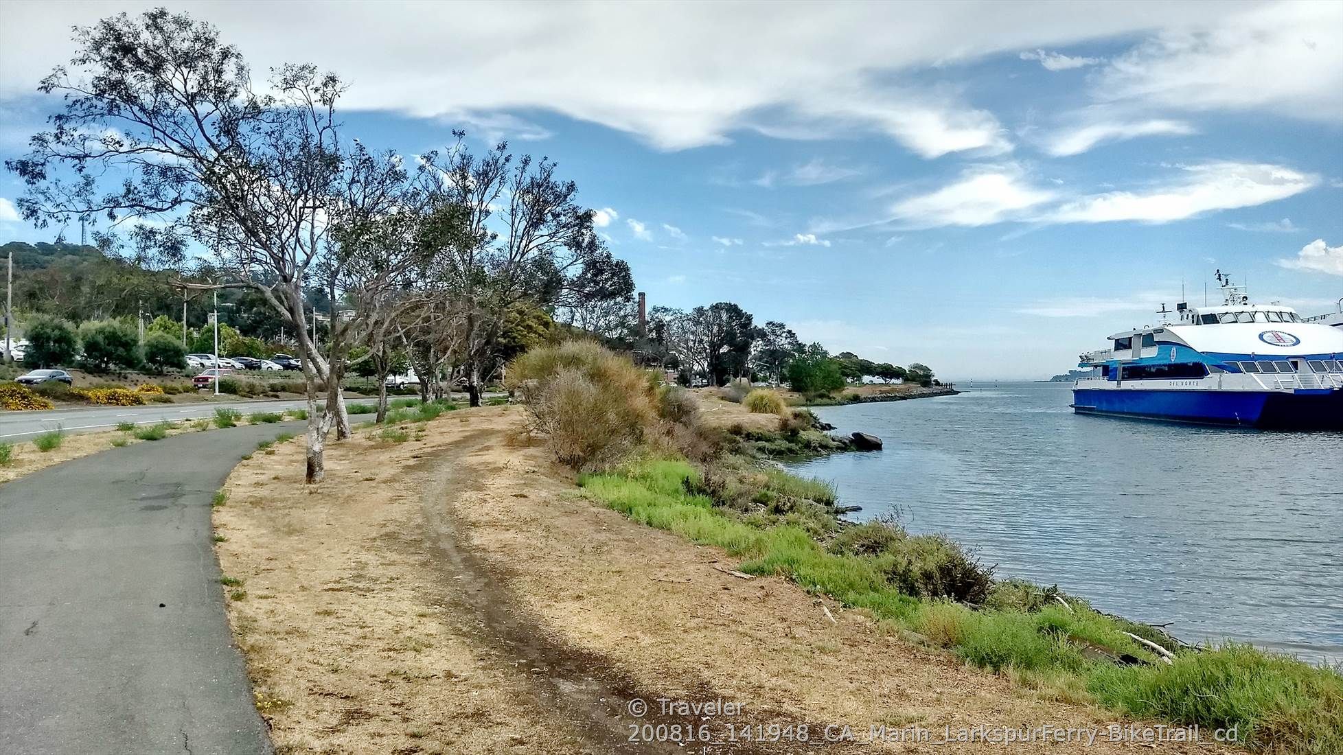 Paved path next to water with a large blue ferry under a bright, cloudy sky. - San Francisco Bay Trail