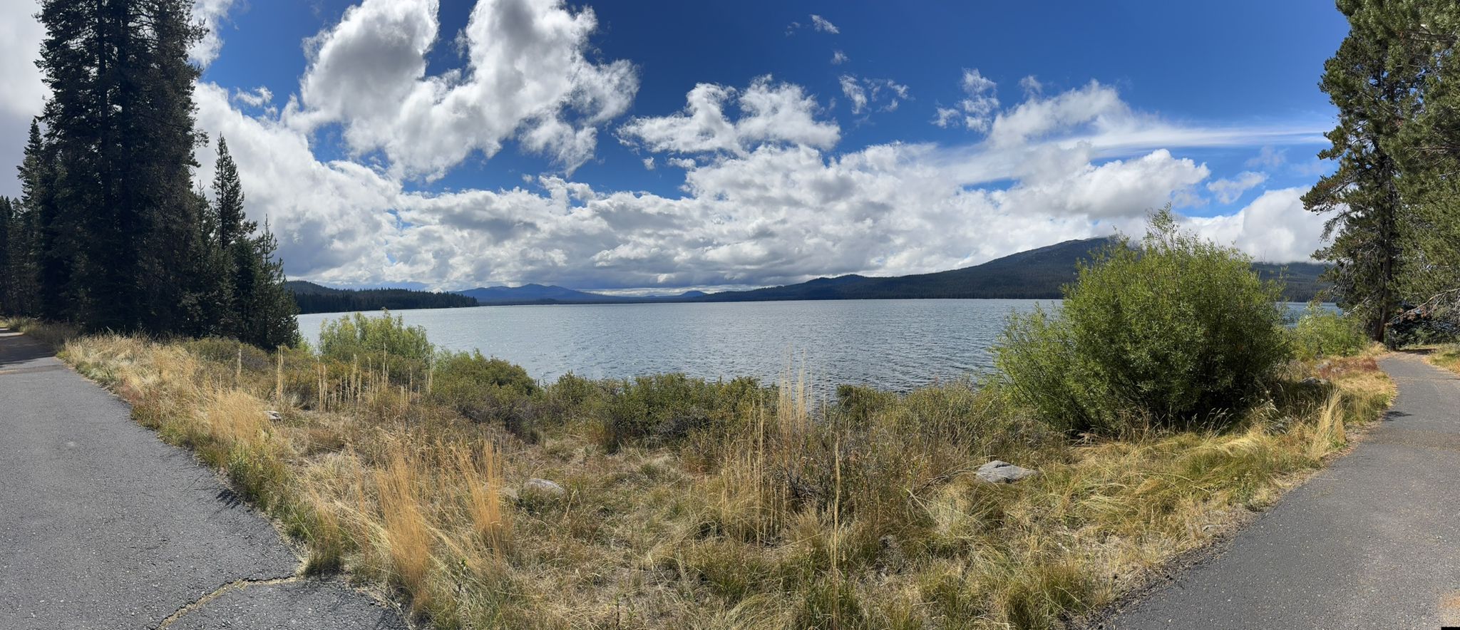 Panoramic view of a large lake, mountains, and roads under a cloudy sky. - Diamond Lake Loop