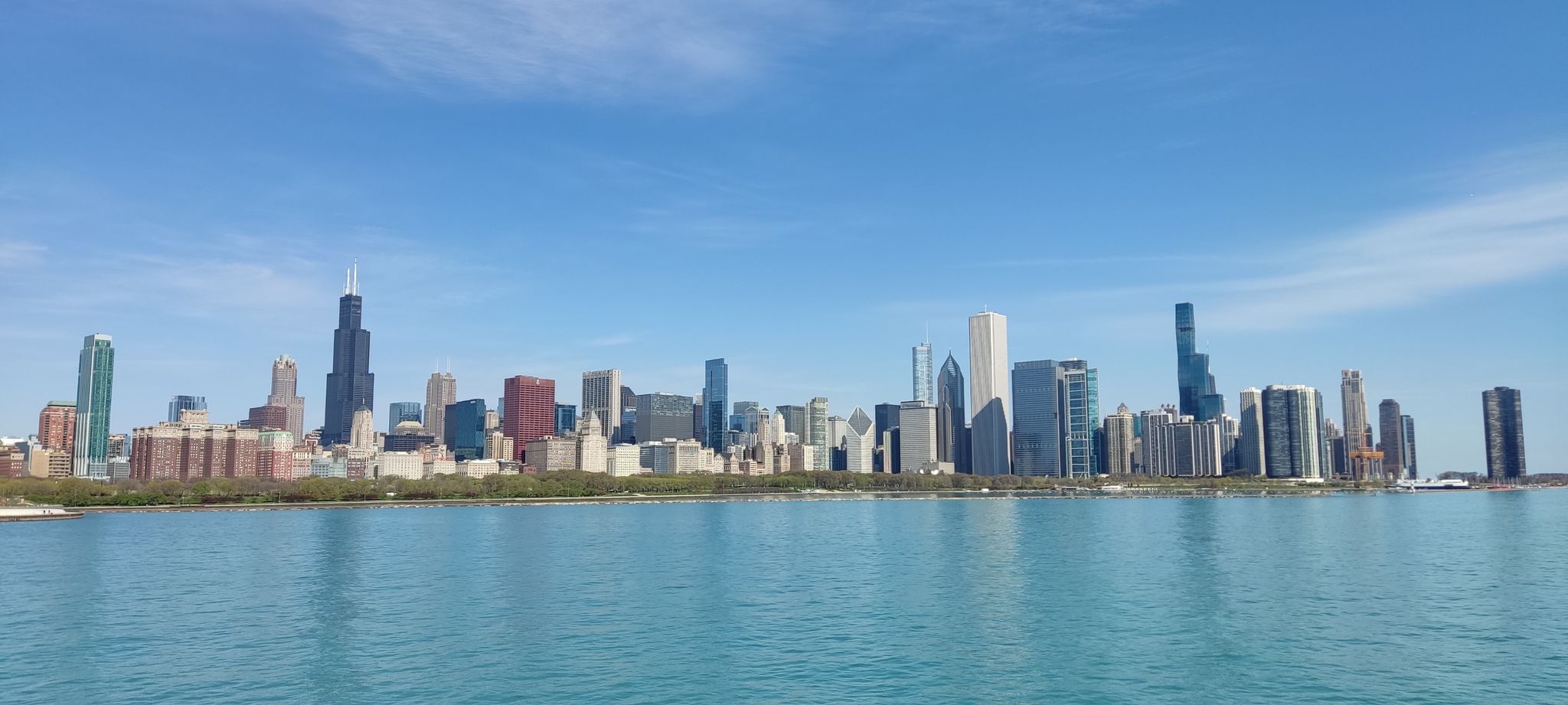 City skyline with tall buildings reflected in calm blue water under a clear sky. - Chicago Lakefront and Riverwalk Trail