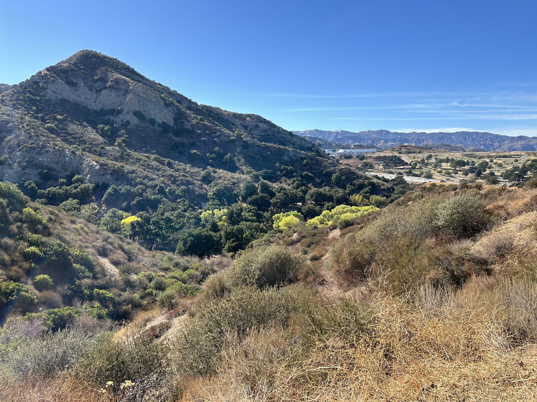 Sunny view of a rugged mountain overlooking a green valley and distant hills. - Santa Clara Trail – Whitney Canyon Park loop from MRCA Open Space