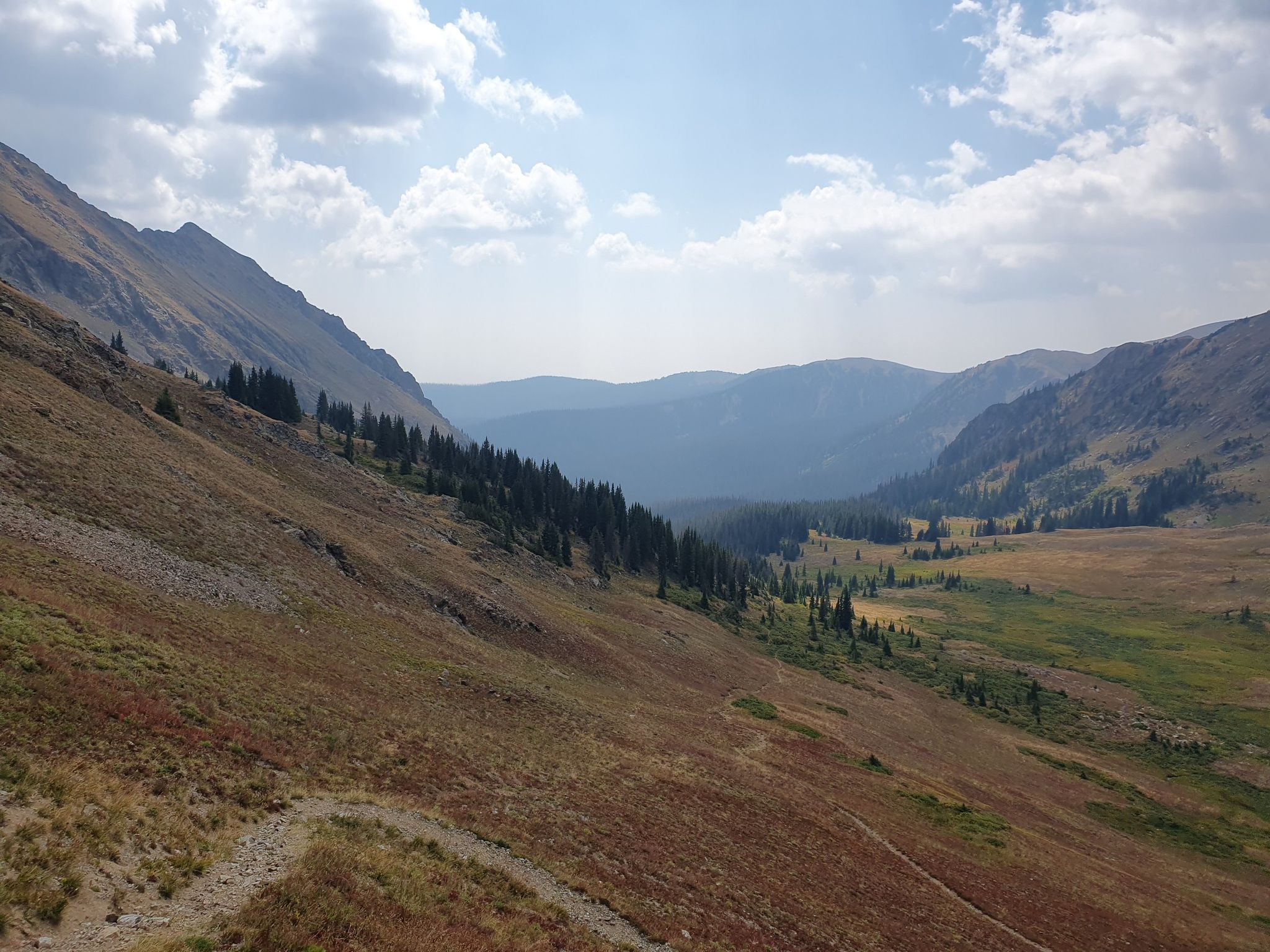 Expansive mountain valley with steep slopes, evergreen trees, and a partly cloudy sky. - Baker Gulch to Bowen Gulch Lake