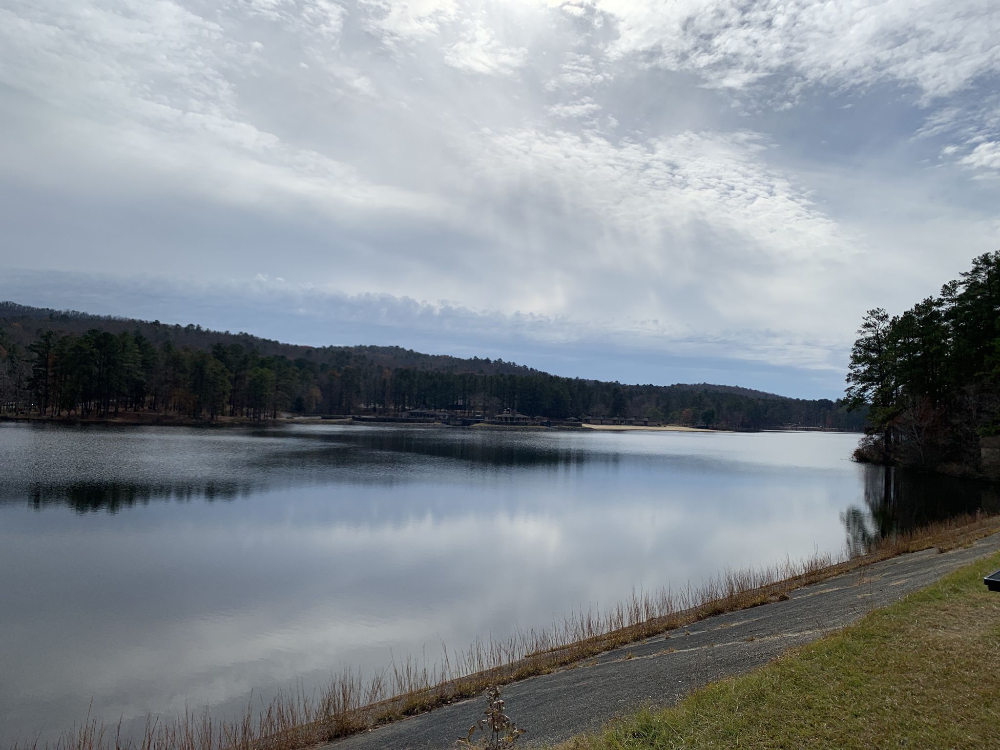 Calm lake reflecting cloudy sky, surrounded by forested hills. - Oak Mountain Red Trail
