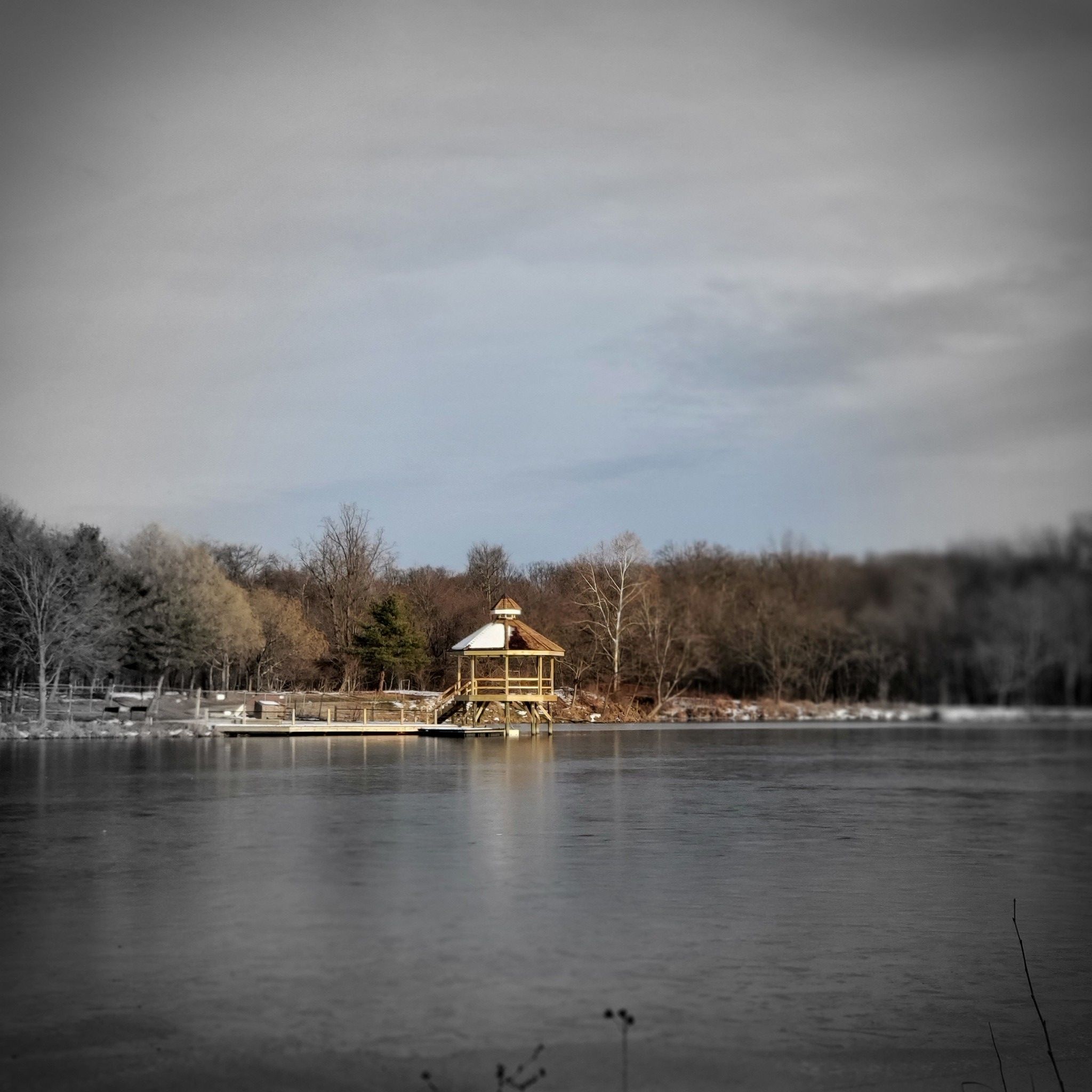 A wooden gazebo on a dock extends into a partially frozen lake. - Paint Branch Trail